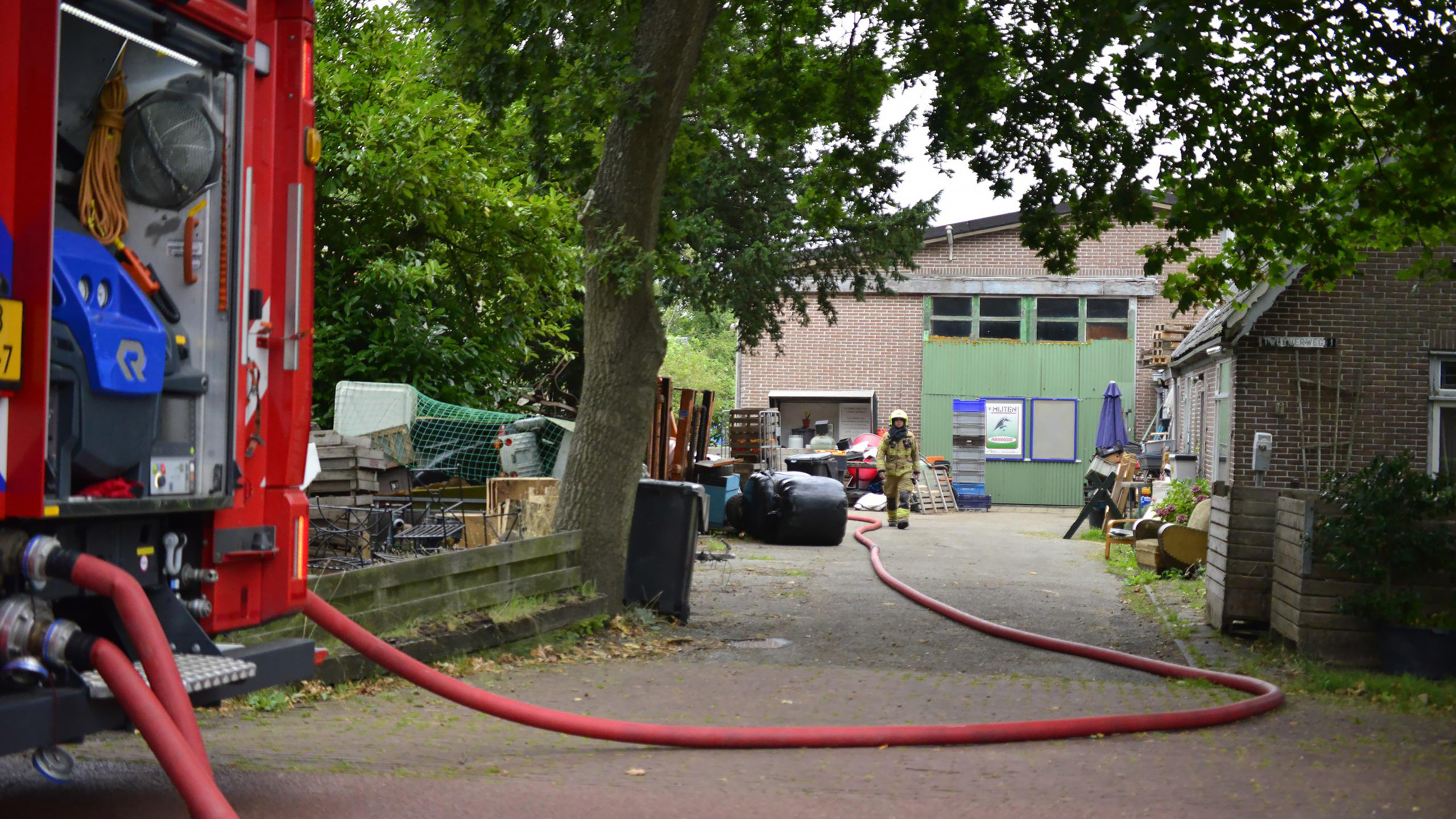 Brandweerwagen en brandweerman met brandslang op een boerenerf.