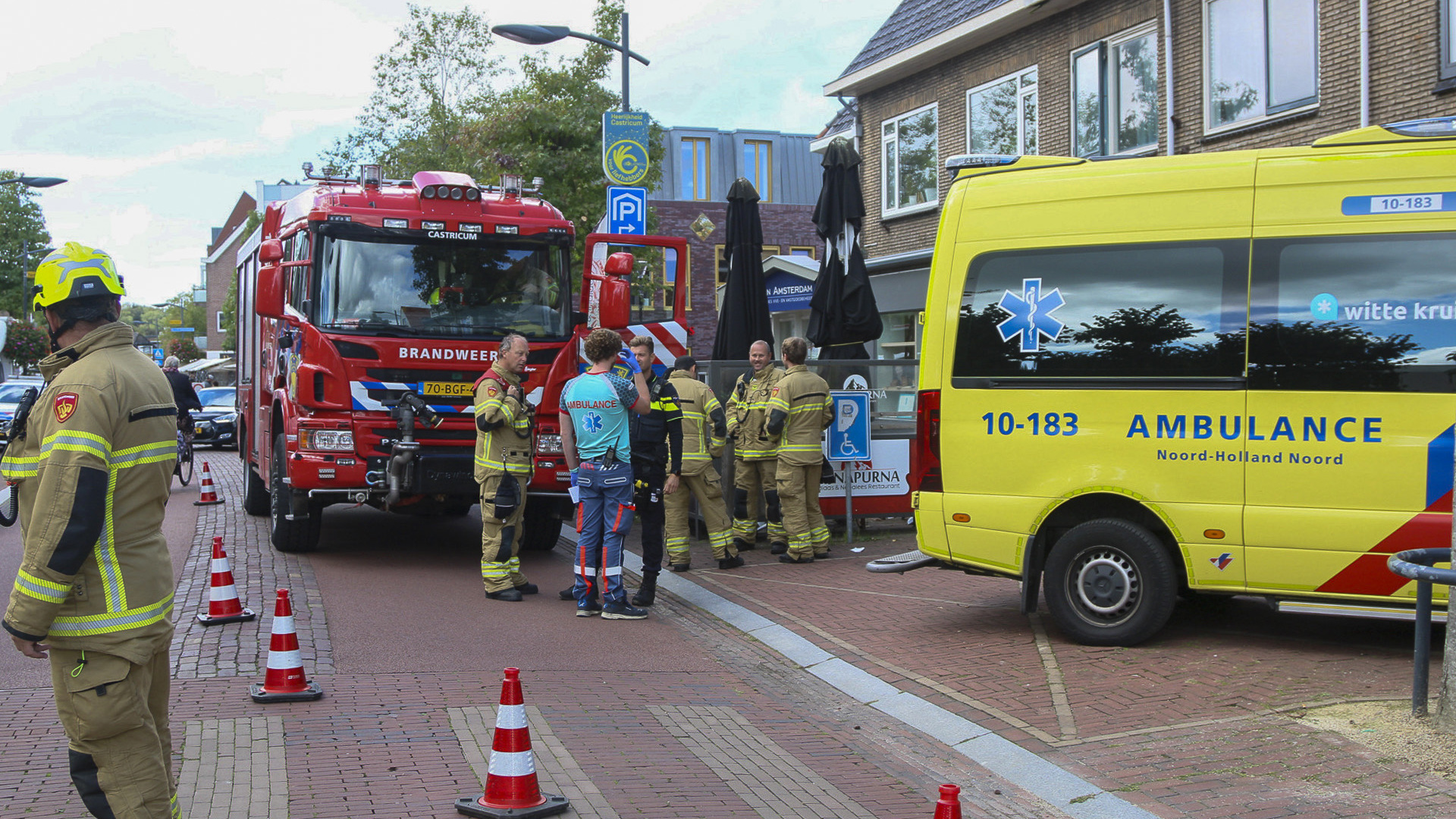 Brandweerwagen en ambulance geparkeerd in een straat, omringd door brandweermannen en medisch personeel.