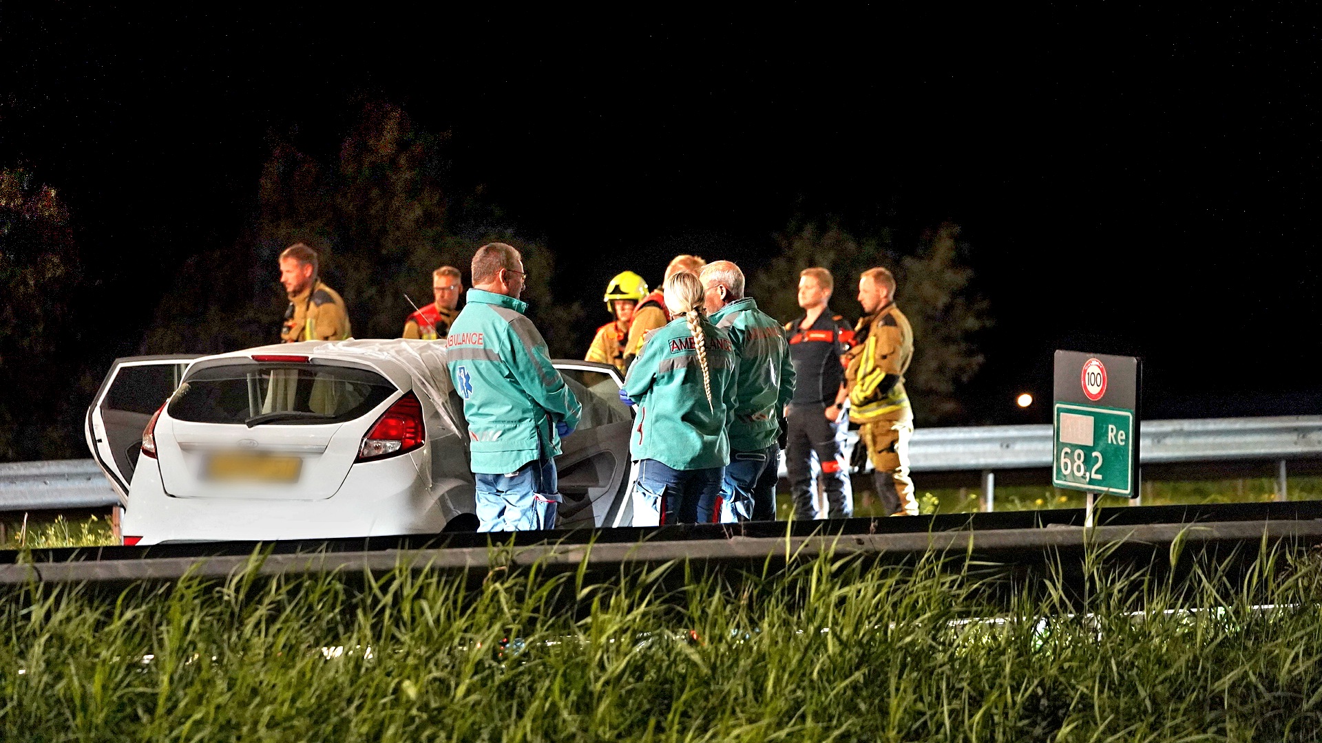 Verkeersongeluk met een witte auto, omringd door hulpdiensten tijdens de nacht op de snelweg bij kilometerpaal 68,2.