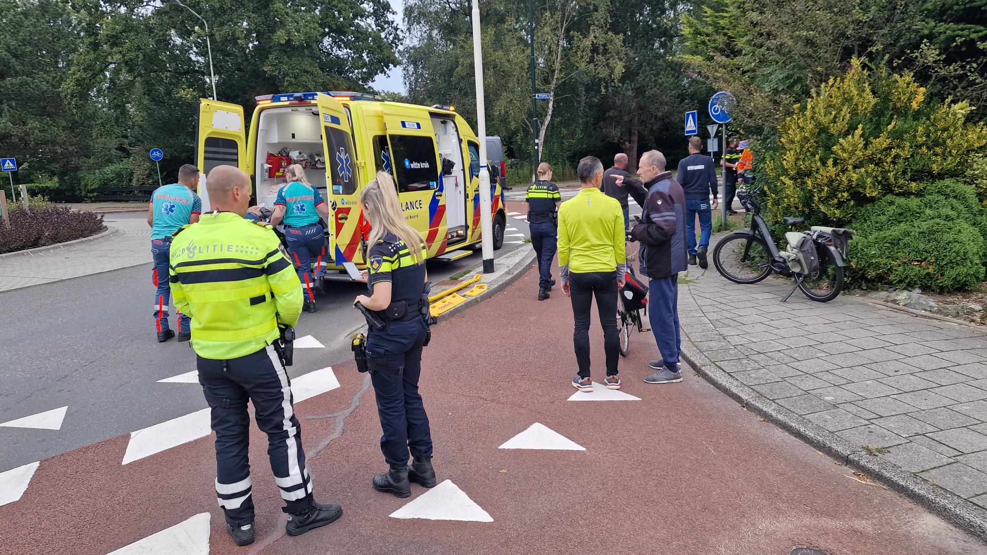 Politieagenten en omstanders bij een verkeersongeluk terwijl ambulancepersoneel een gewonde in een ambulance plaatst.