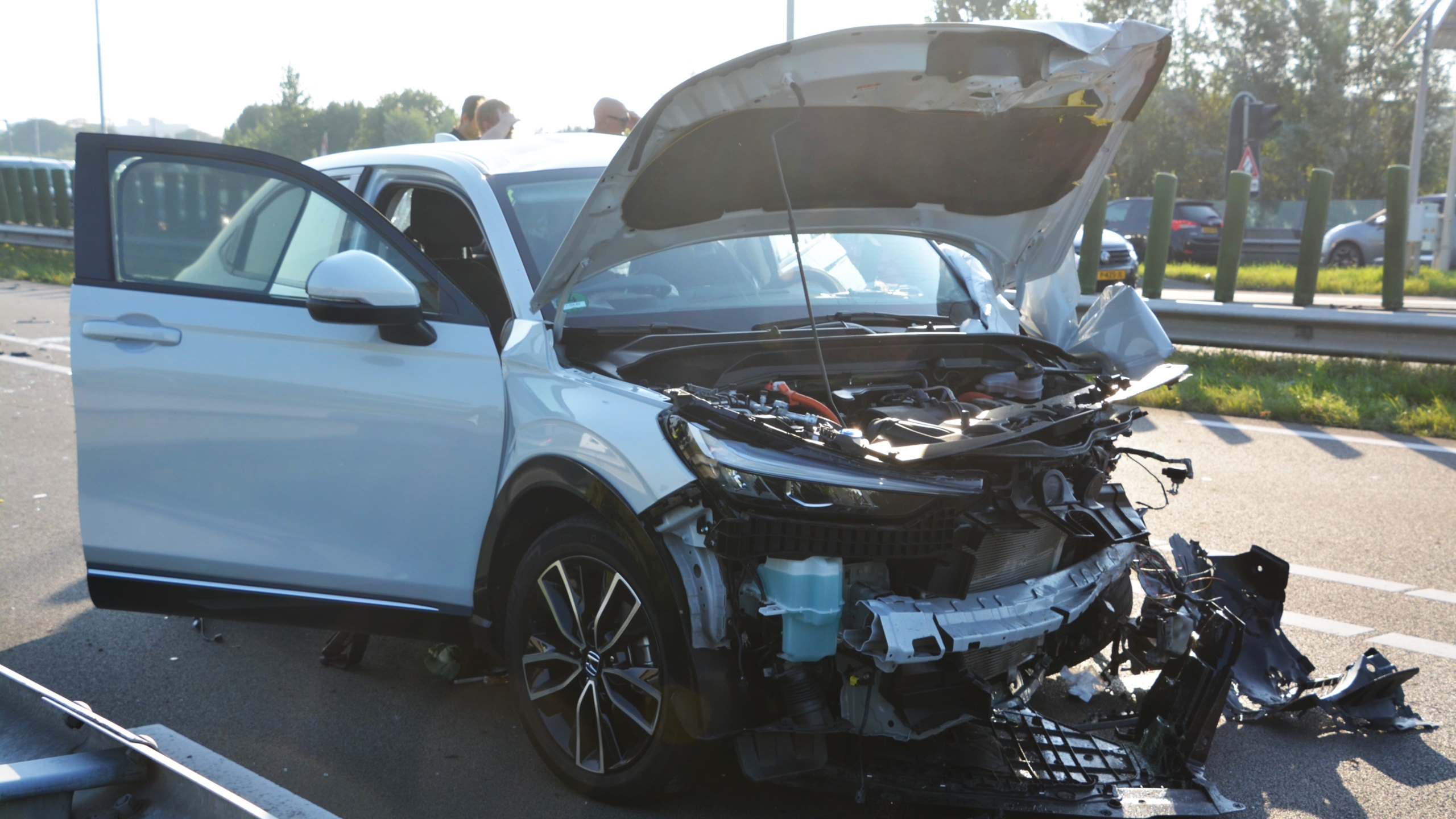 Auto met ernstige schade aan de voorkant en open motorkap na een ongeval, geparkeerd op de weg met geopende bestuurdersdeur.