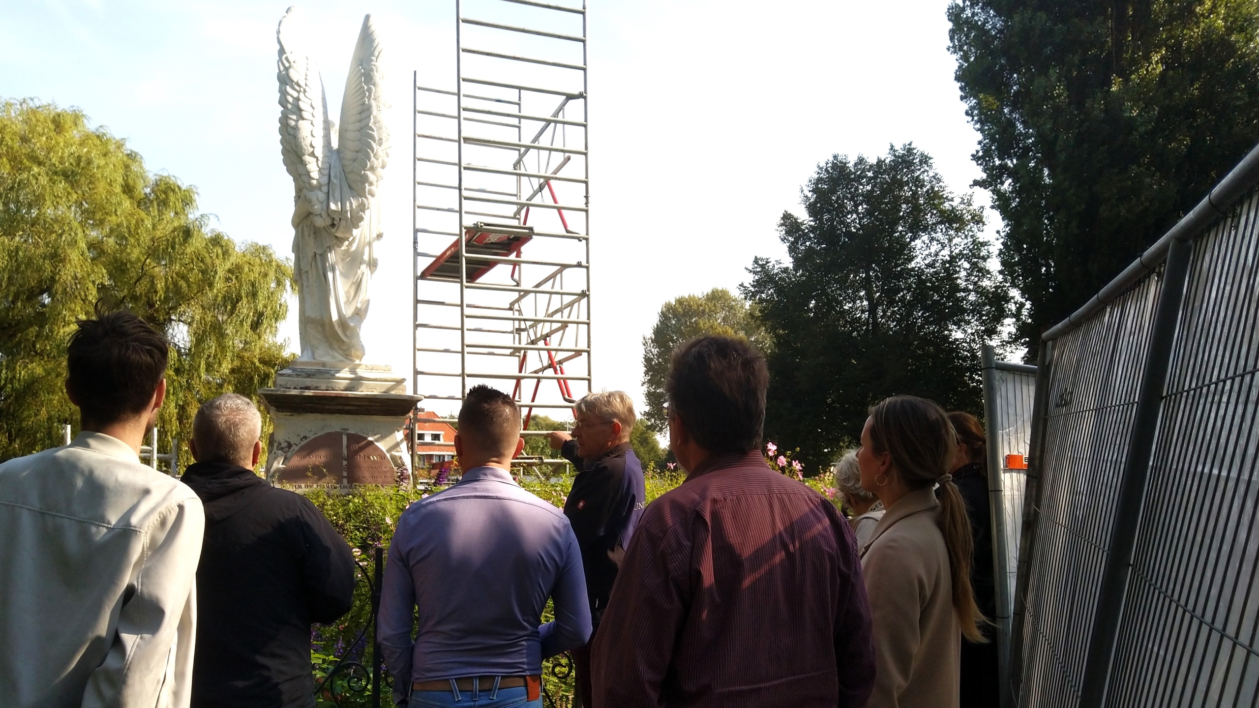 Mensen staan voor een engelstandbeeld met een steiger ernaast.