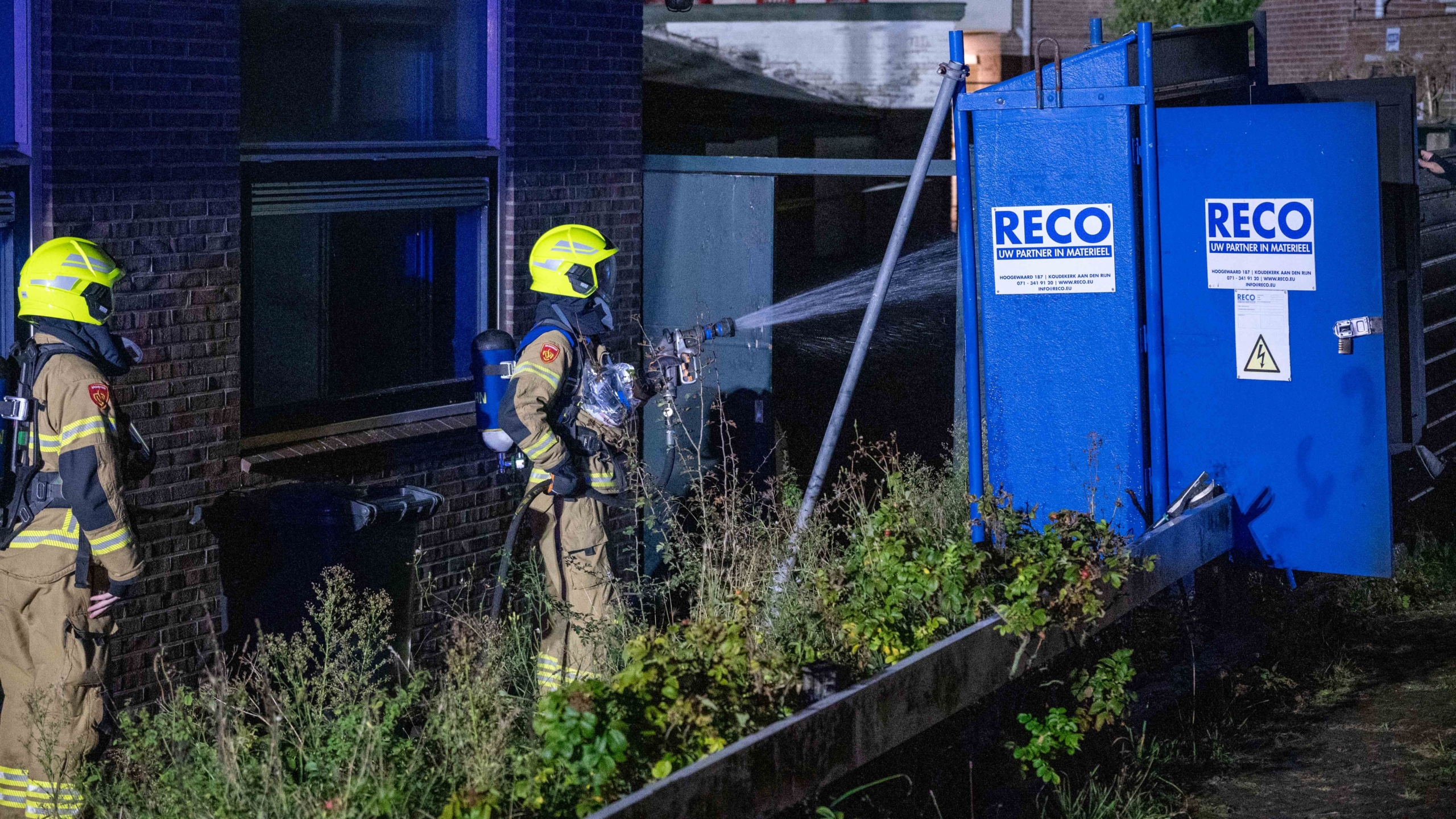 Brandweerlieden in actie bij een elektriciteitskast met RECO-logo.