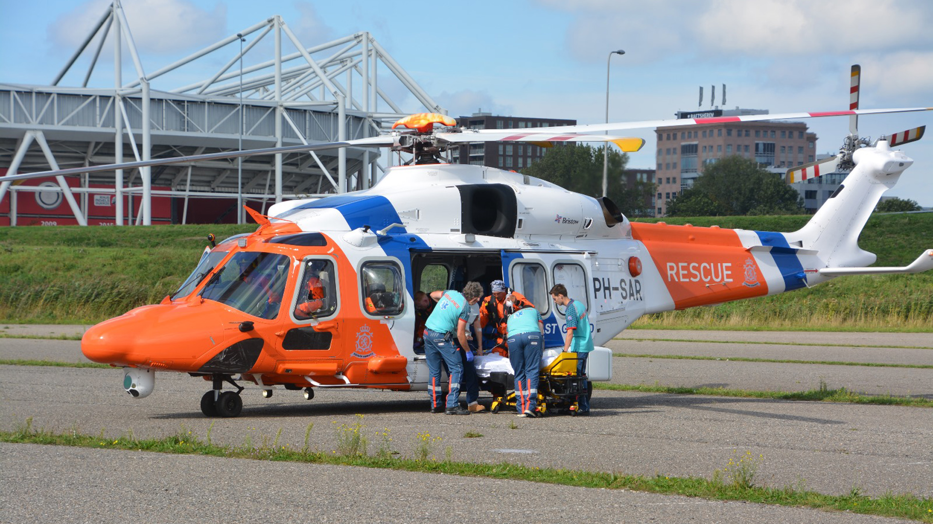 Reddingshelikopter op de grond met personeel dat een brancard naar binnen brengt.