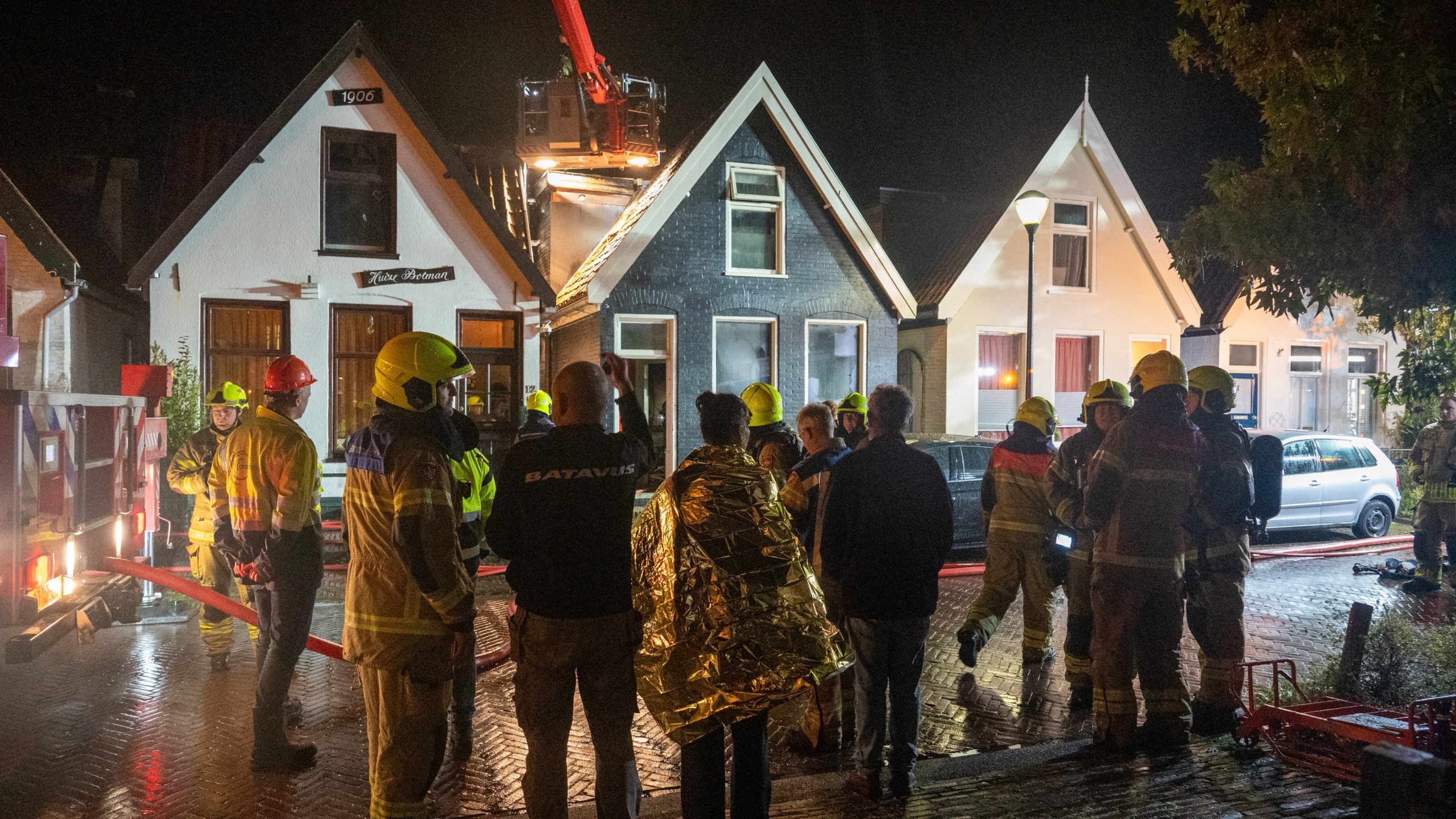 Brandweerlieden en omstanders voor huizen tijdens een nachtelijke brandweeroperatie.