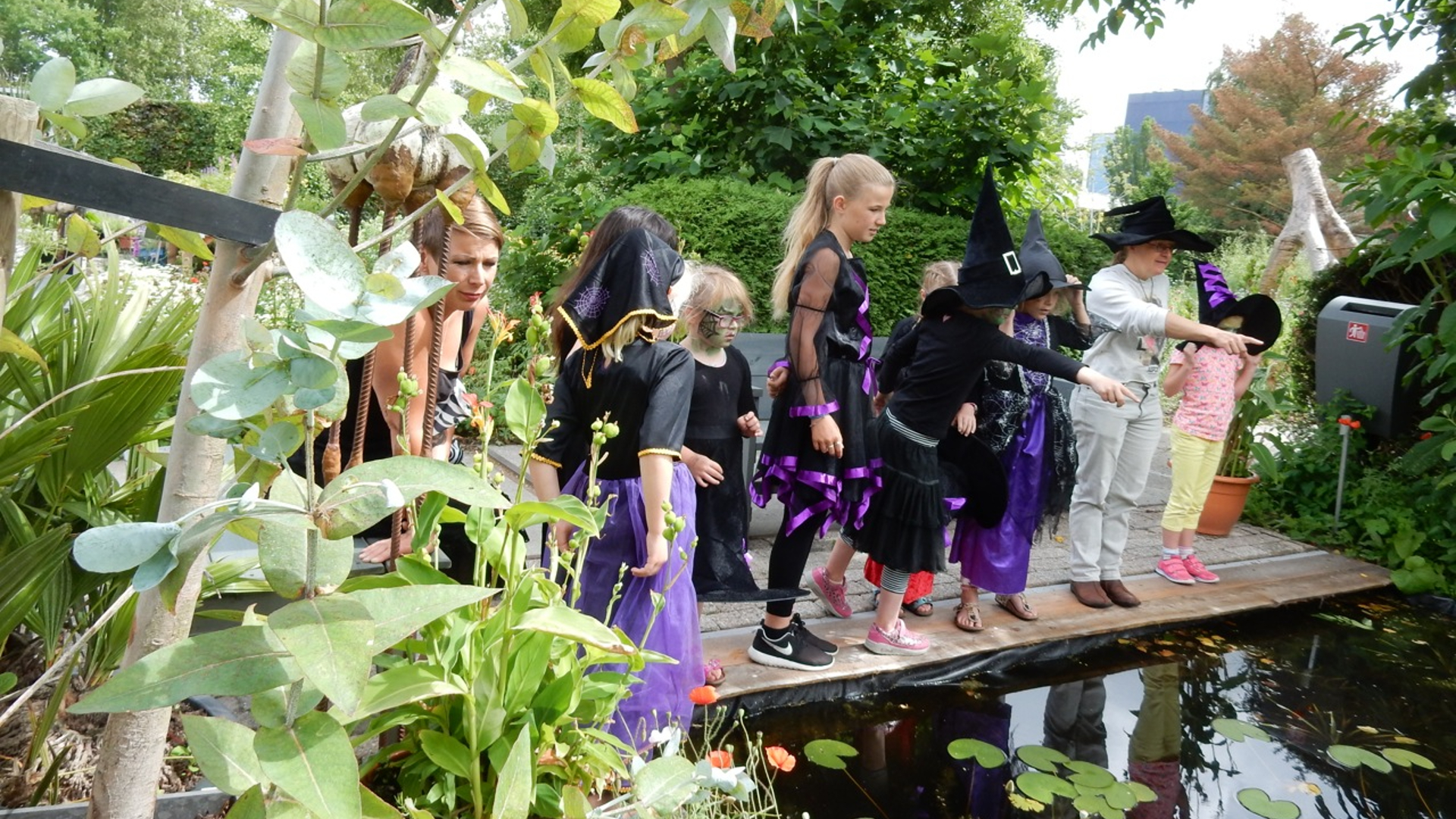 Kinderen verkleed als heksen kijken naar een vijver in een tuin.