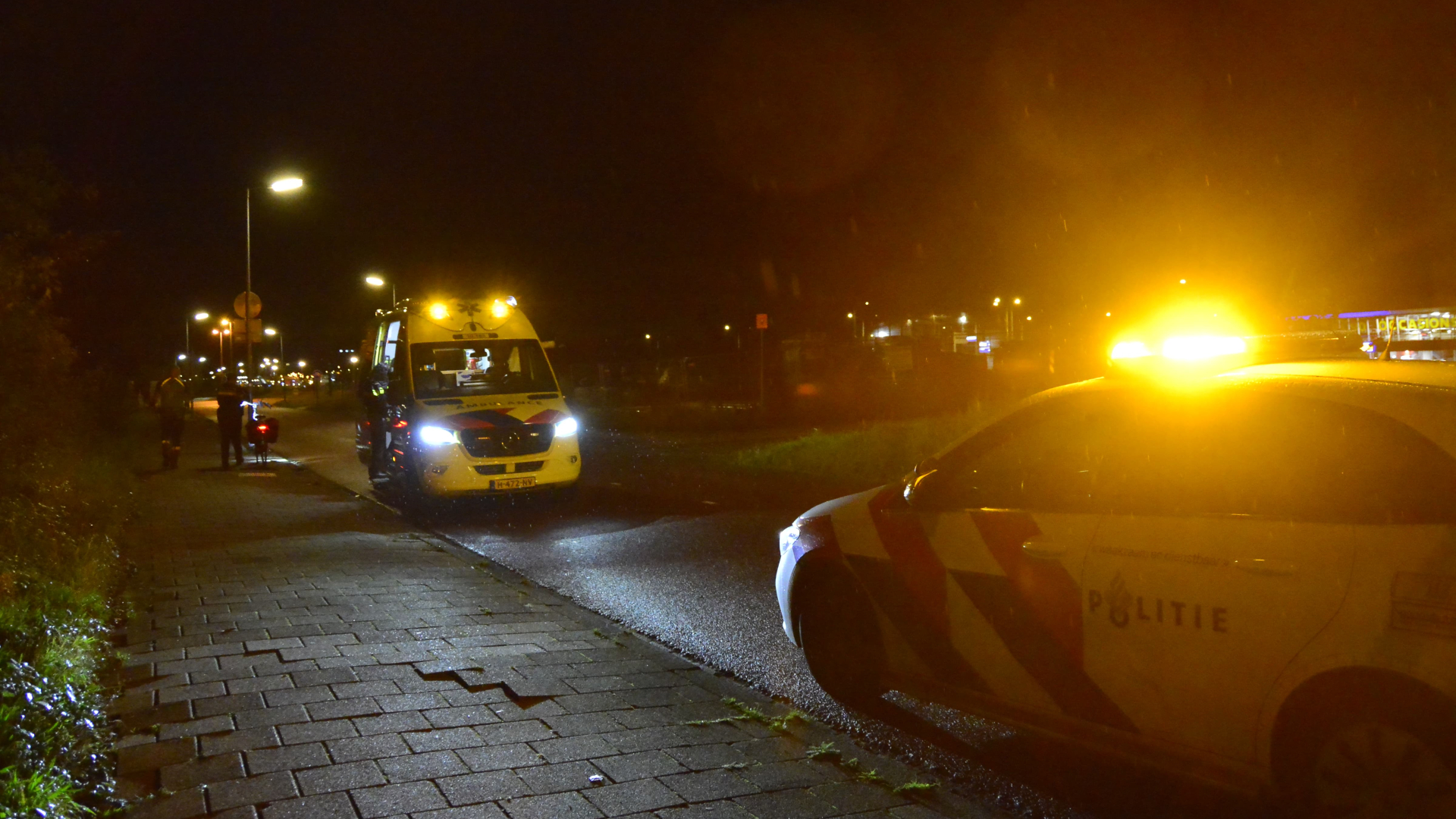 Politie- en ambulancevoertuigen met knipperende lichten op een donkere straat.