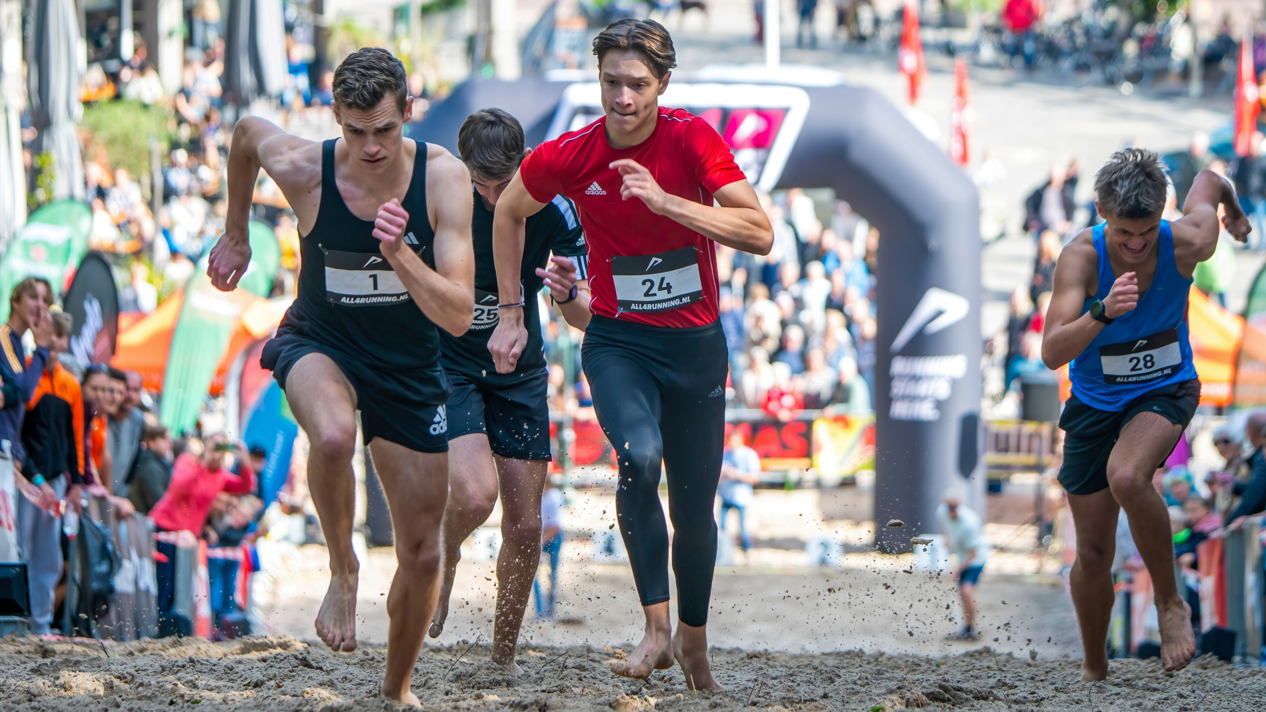 Hardlopers nemen deel aan een zandrace met publiek op de achtergrond.