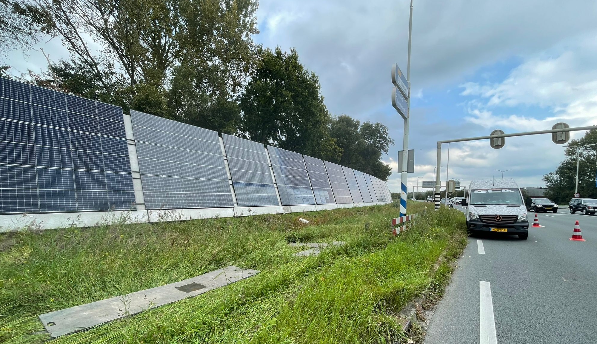 Zonnepanelen langs de kant van een weg met een geparkeerde bestelwagen en verkeerskegels op een bewolkte dag.