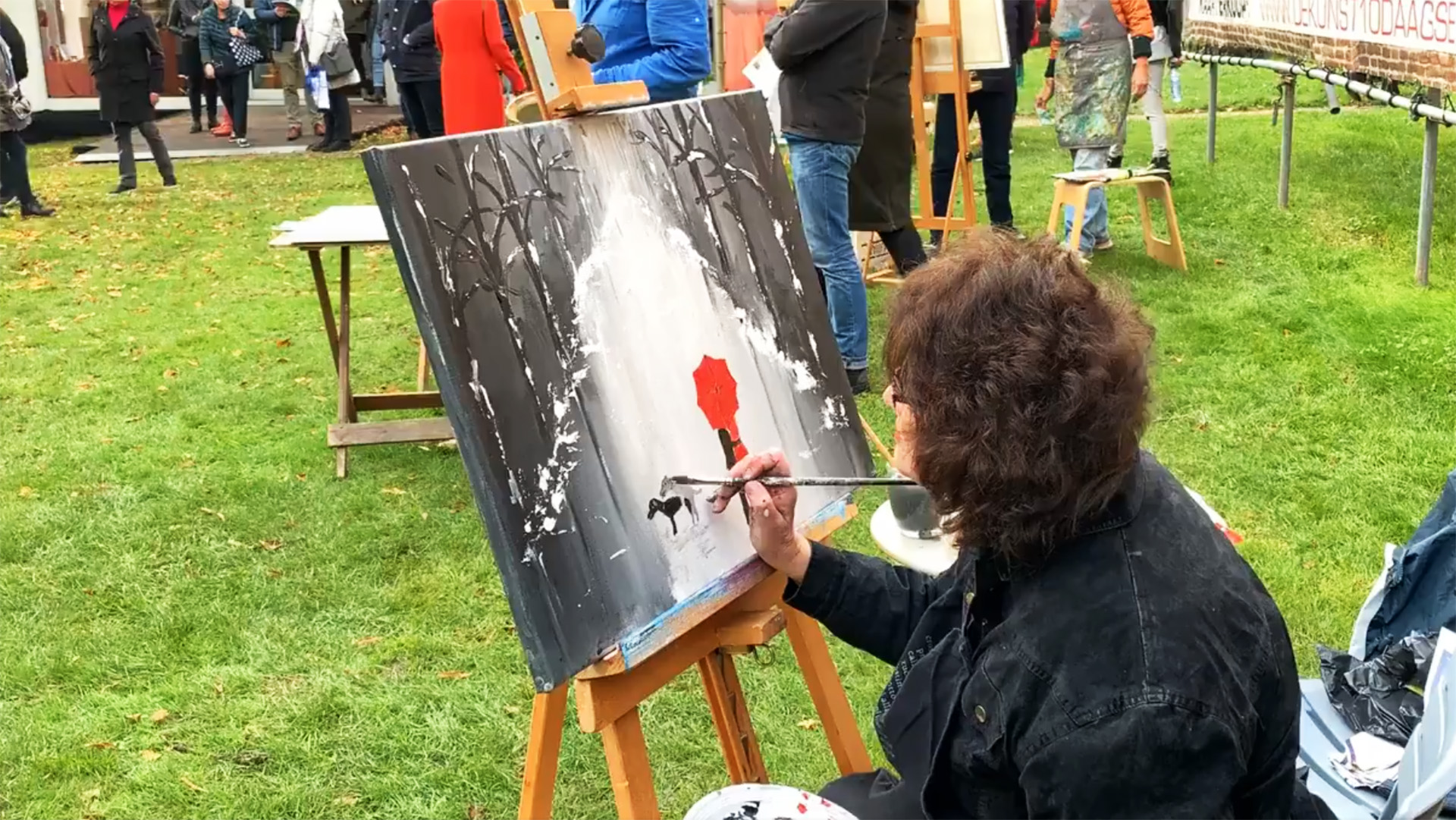 Kunstenares schildert een landschap met een persoon met een rode paraplu tijdens een buiten schilderfestival.