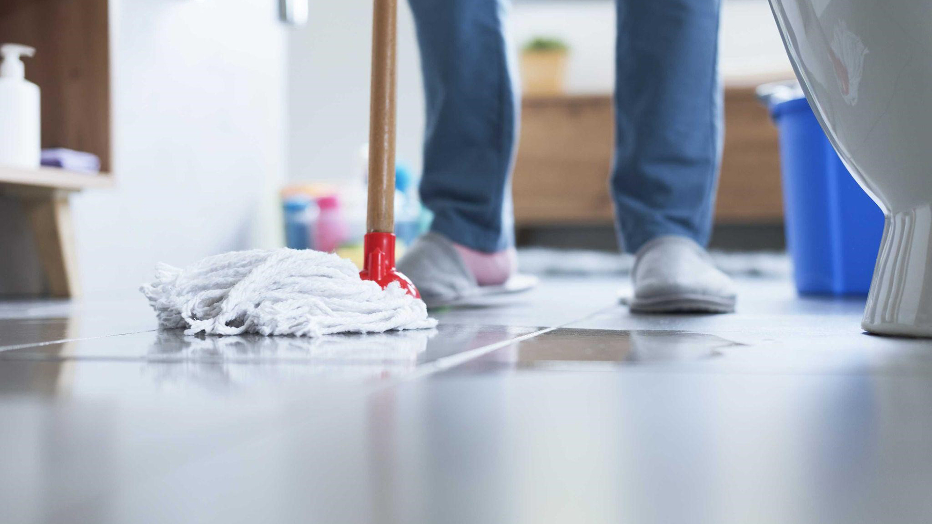 Persoon die de vloer dweilt met een witte mop in een badkamer.