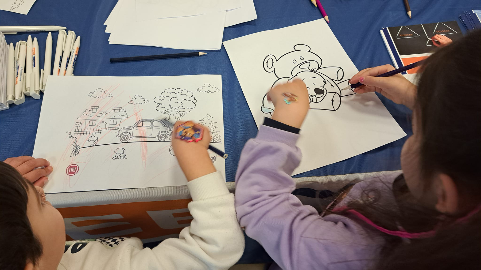 Kinderen kleuren verschillende tekeningen in op een tafel met kleurpotloden en pennen.