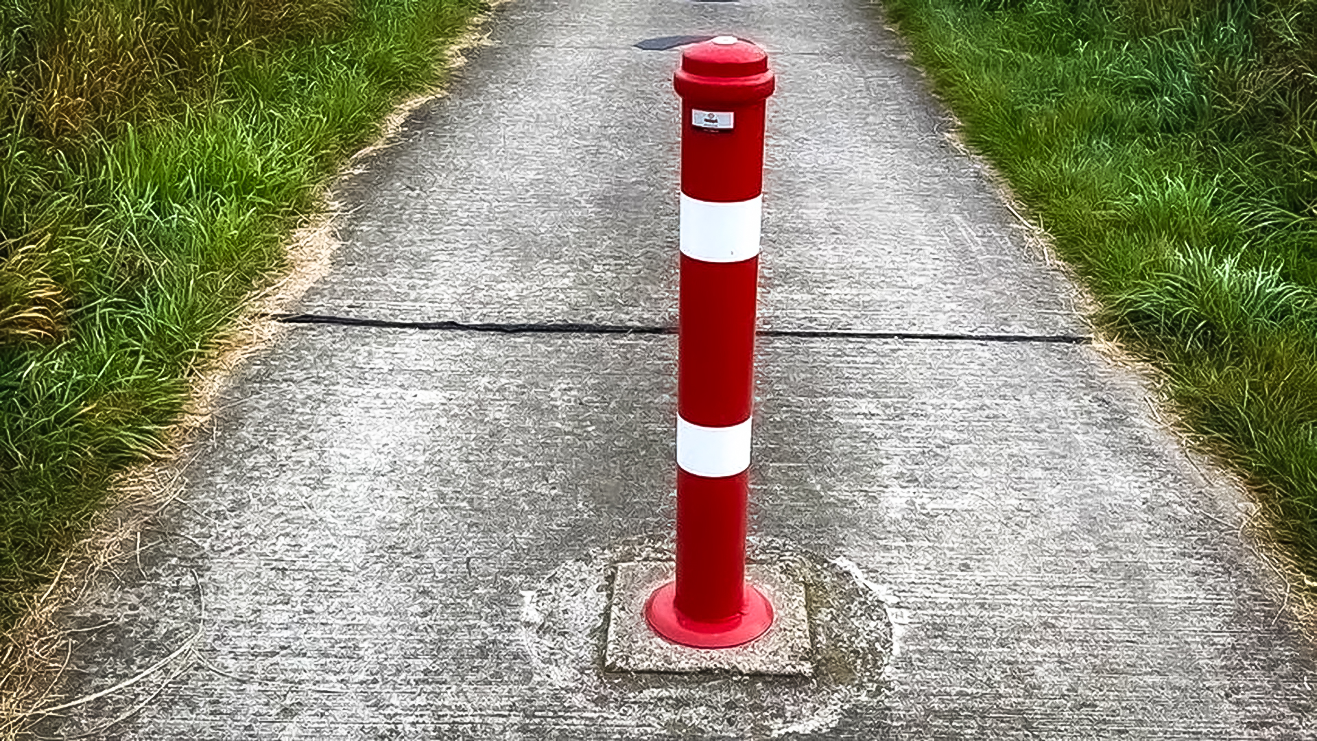 Rode paal met witte strepen op een betonnen pad omringd door gras.