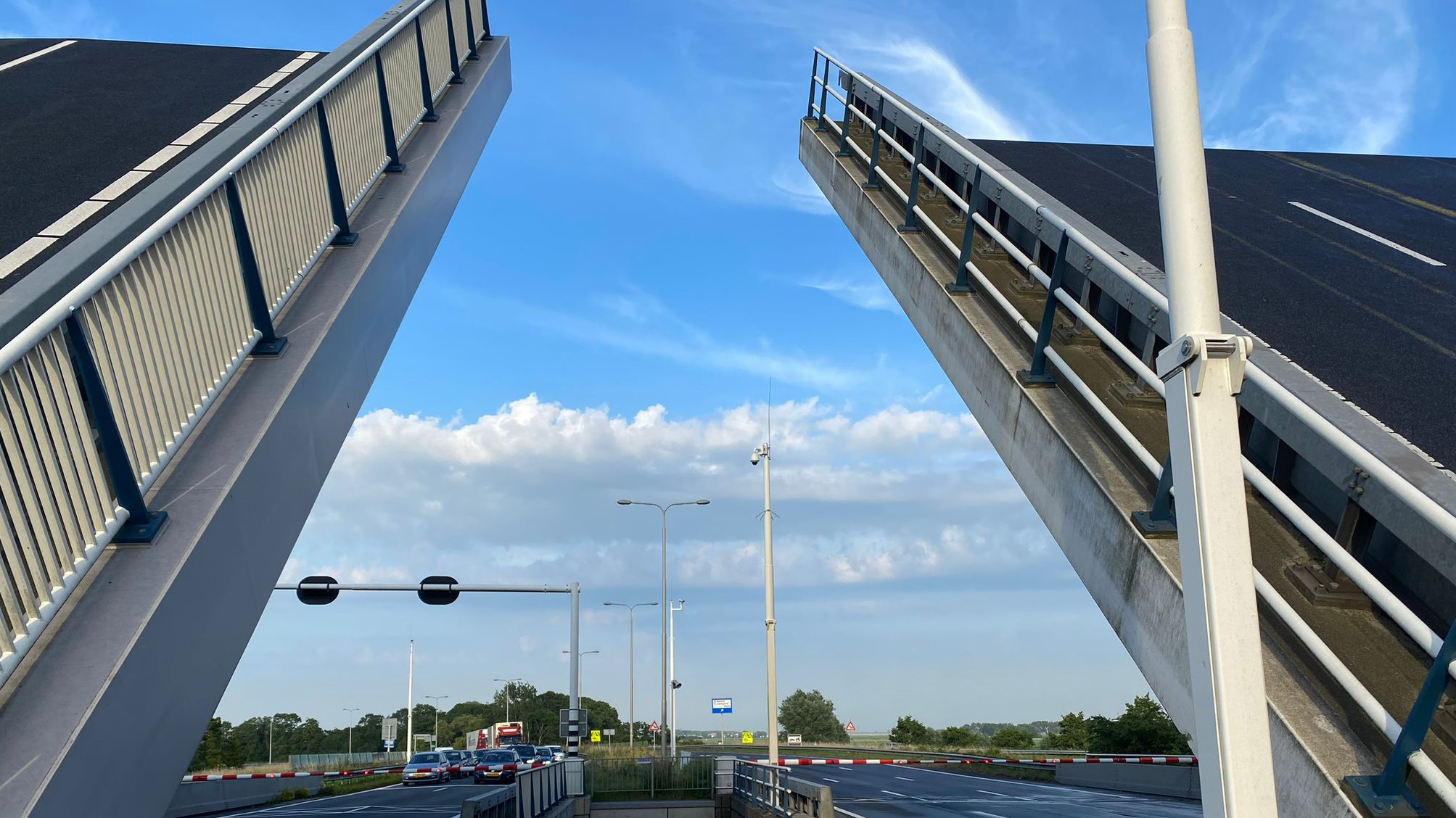 Een opgehaalde brug met auto's en verkeersborden zichtbaar op de achtergrond.