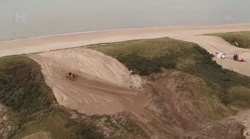 Luchtfoto van een bulldozer die zand verplaatst op een duin nabij een strand.