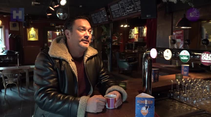 Man in leren jas met schapenvacht zit met een kop koffie aan een bar in een cafe.