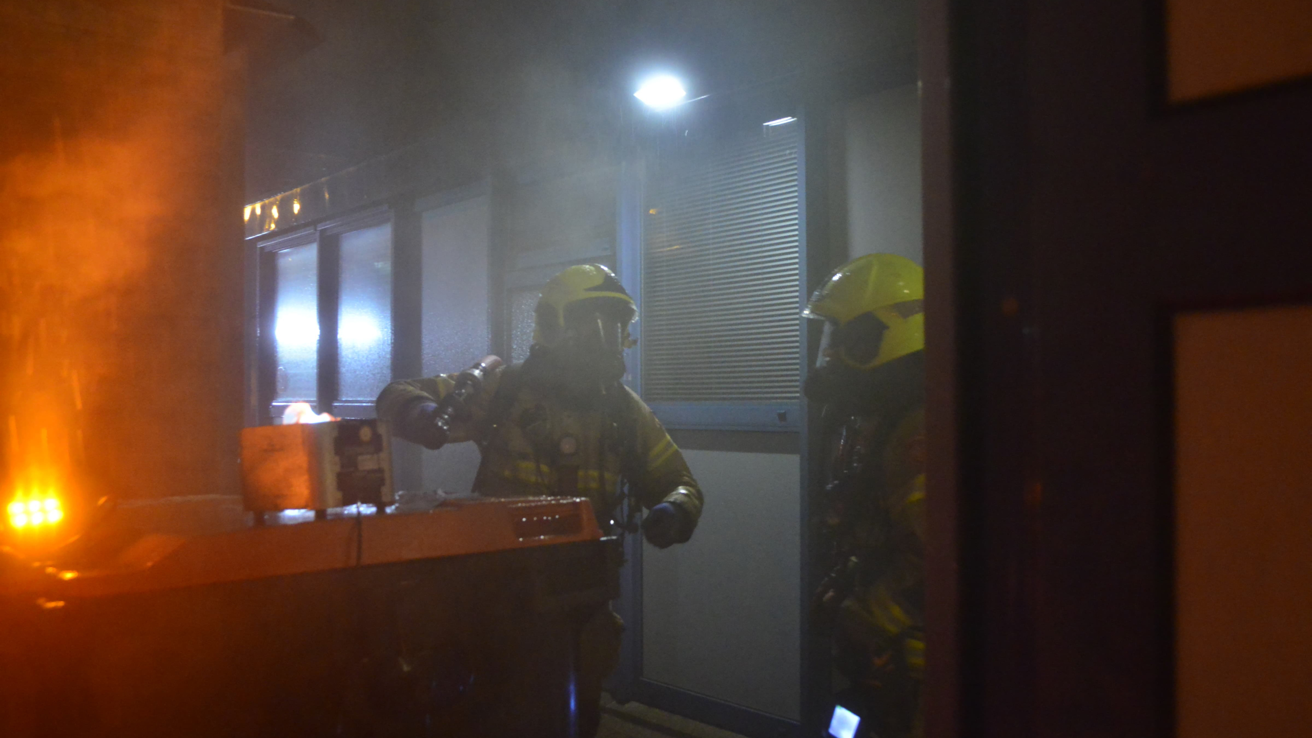 Brandweerlieden blussen 's nachts een brand in een container.