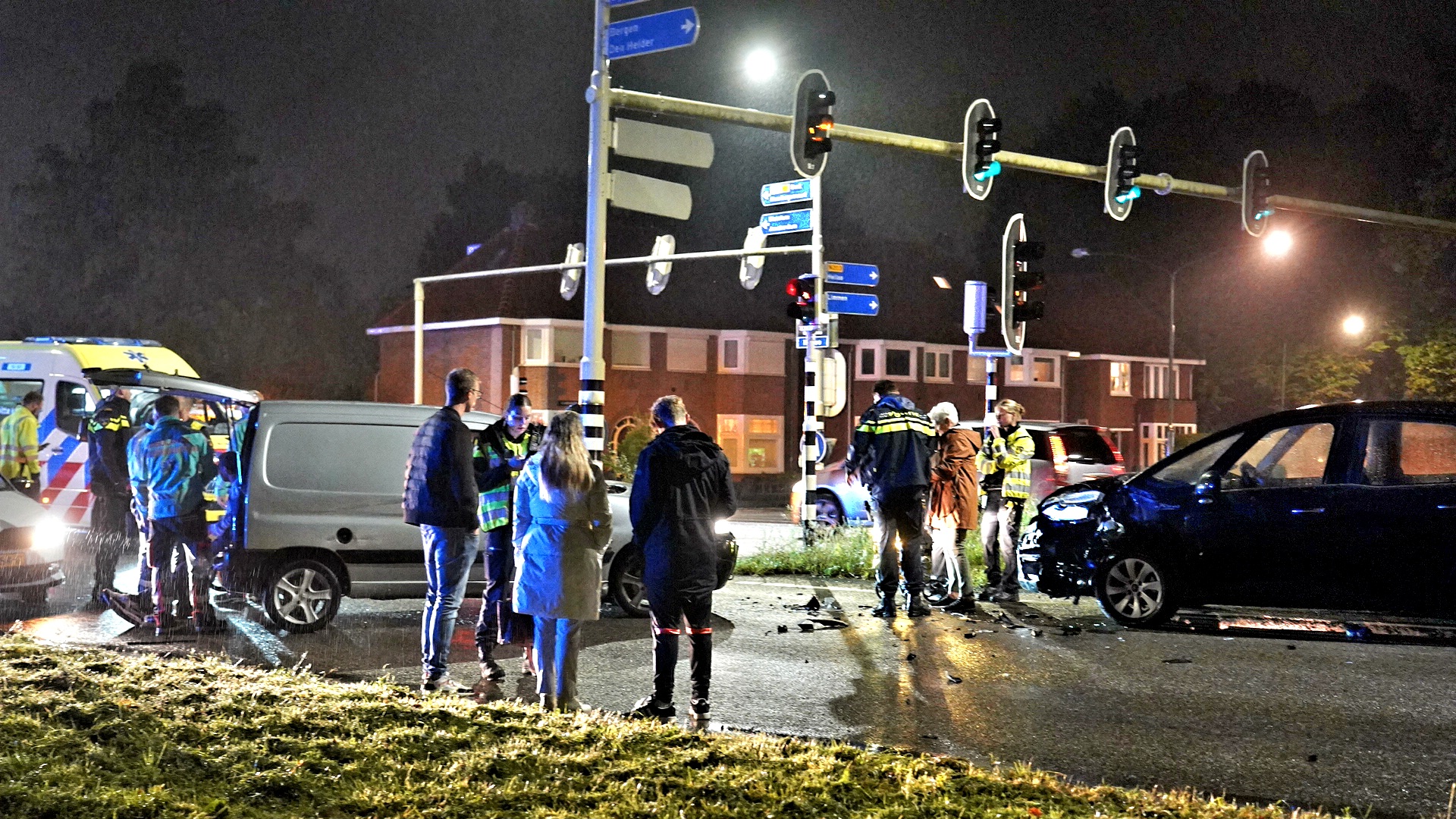 Verkeersongeluk bij een kruispunt in de avond met politie, ambulance en omstanders.