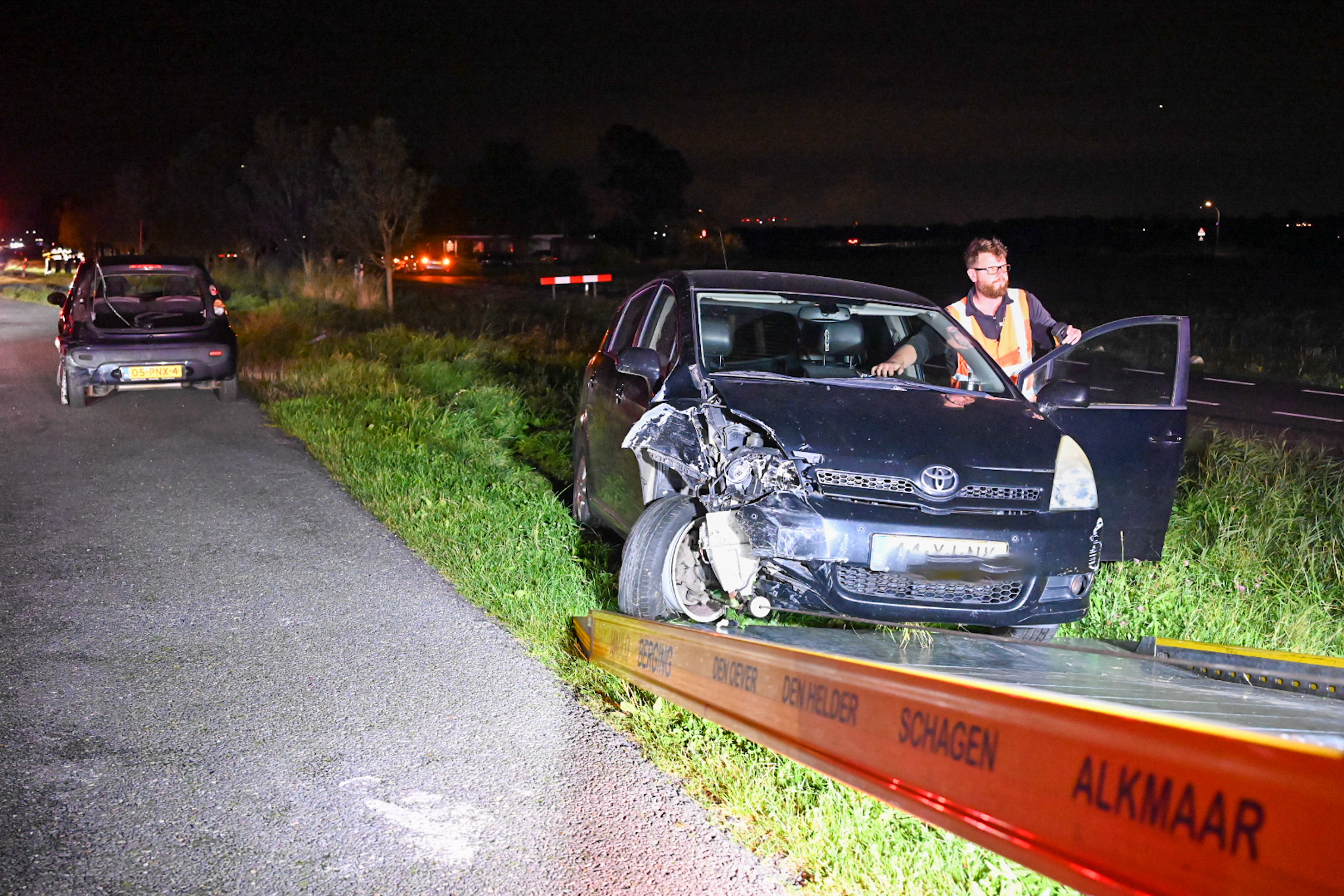 Autowrak na ongeval met berger en man in hesje op een weg 's nachts.