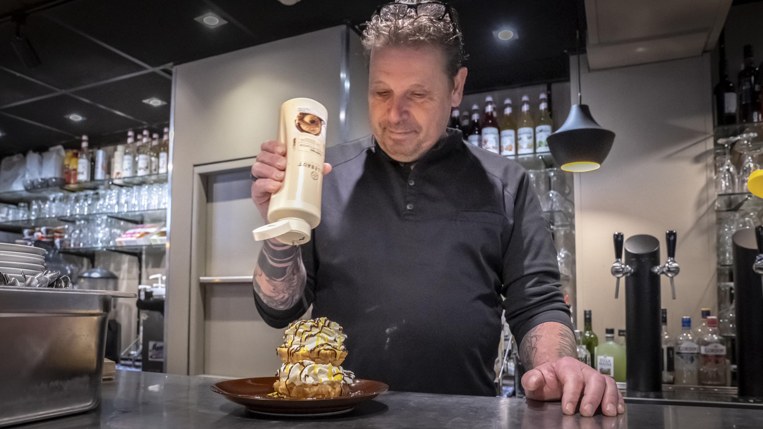 Man decoreert wafel met room in een keuken.