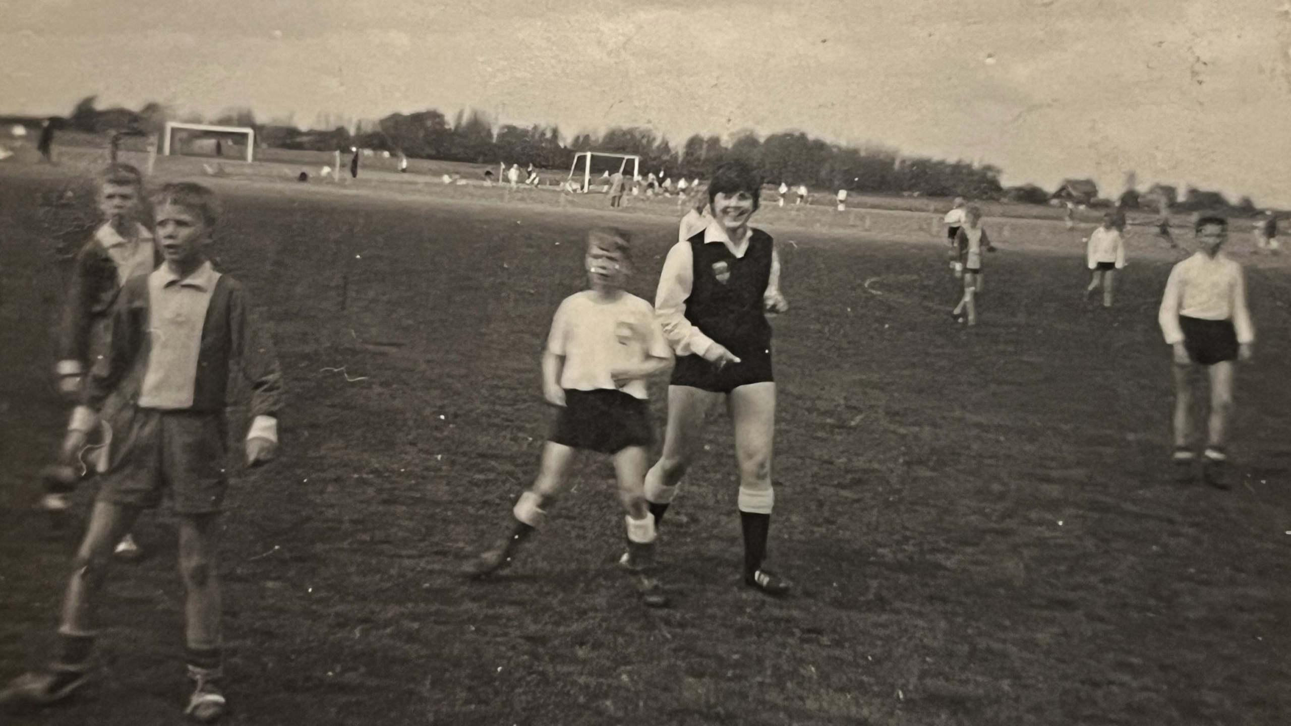 Zwart-wit foto van een groep jonge voetballers op een veld met doeltjes op de achtergrond.