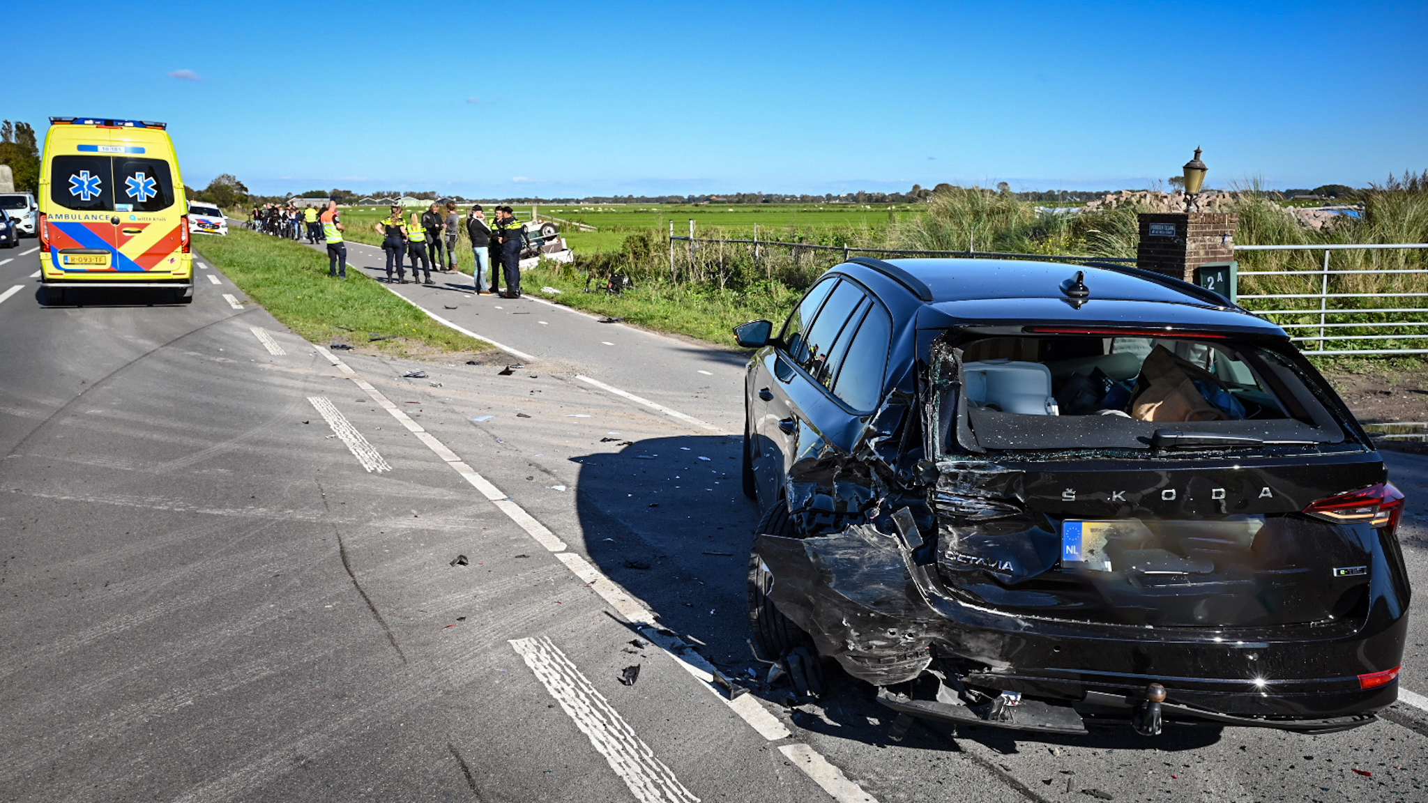 Verkeersongeval met blikschade aan de achterkant van een zwarte Škoda, met een ambulance en hulpverleners op de achtergrond.