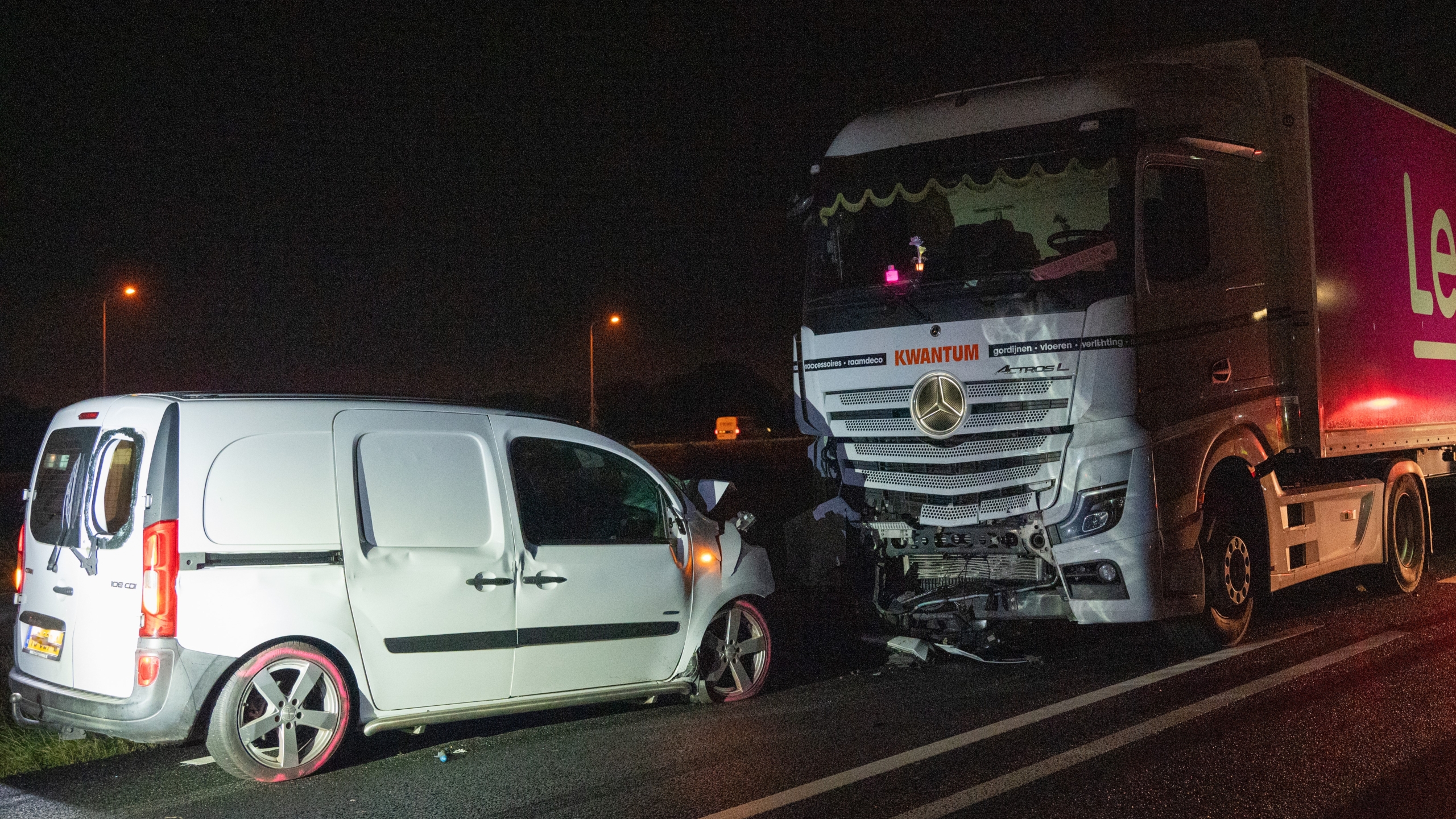 Witte bestelwagen botst tegen vrachtwagen op de snelweg 's nachts.