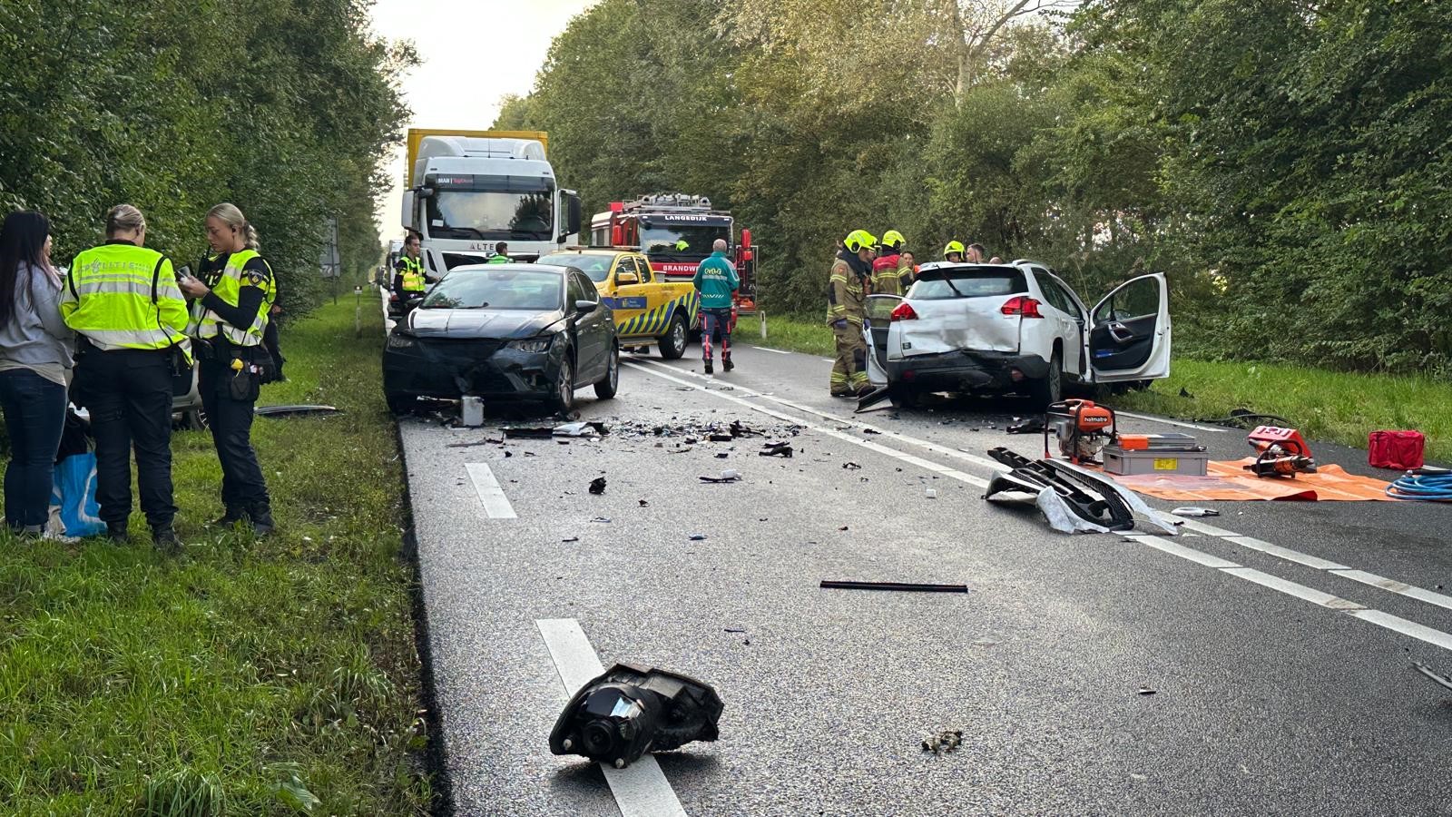 Verkeersongeval op een weg met twee beschadigde auto's, omringd door politie, brandweer en hulpdiensten.