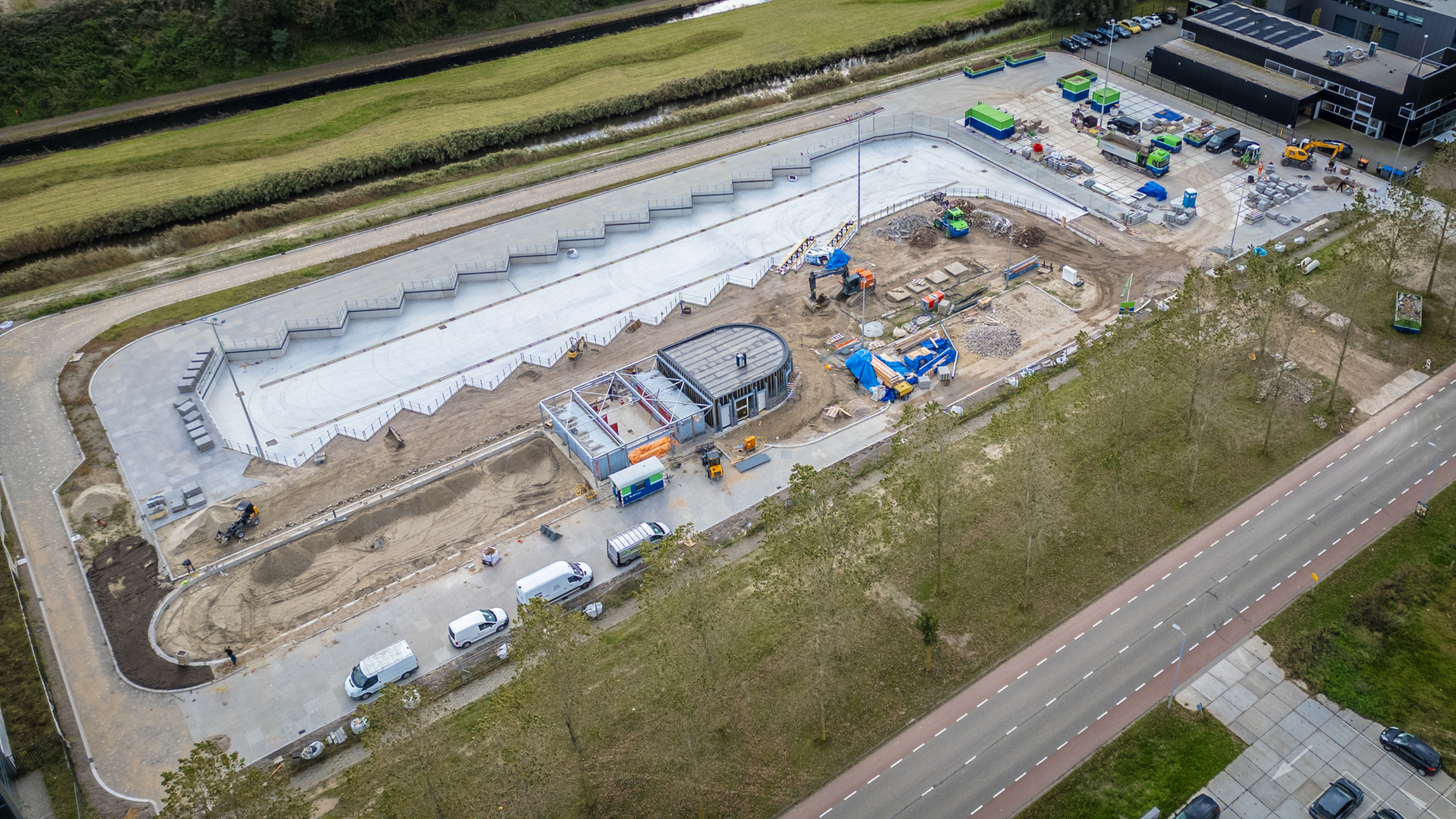 Luchtfoto van een bouwterrein met een zigzagvormige structuur en gebouw in aanbouw omringd door machines en voertuigen.