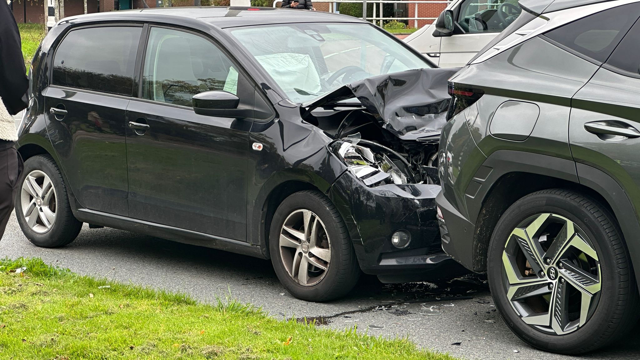 Zwarte auto met zware schade aan de voorkant na botsing met grijze SUV op de weg.