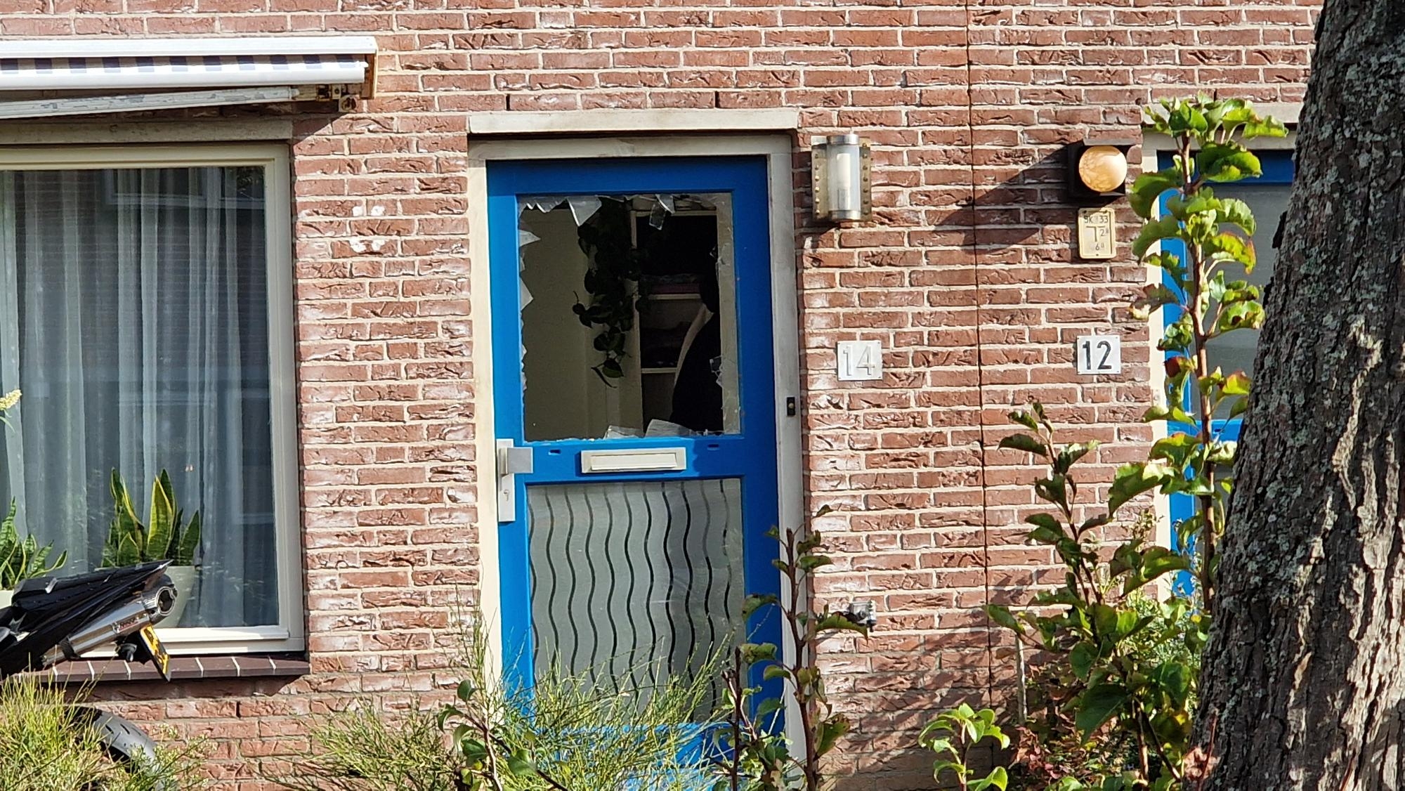 Een huis met een beschadigde deur met een kapot raam, huisnummer 14 zichtbaar.