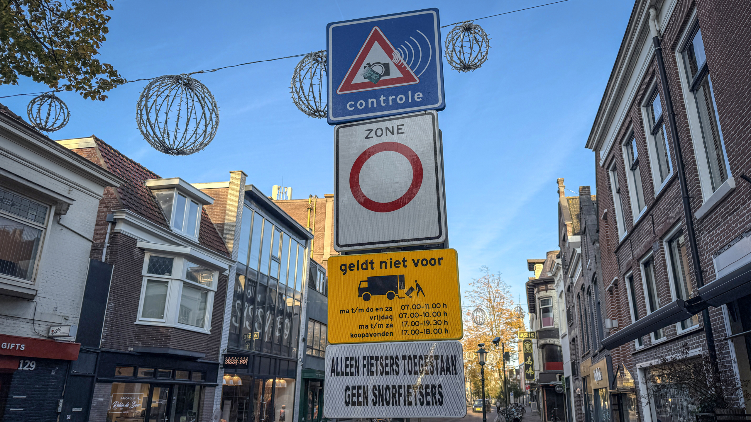 Verkeersbord met toegangsbepalingen op een straat in een stadscentrum, met omliggende huizen en winkels.