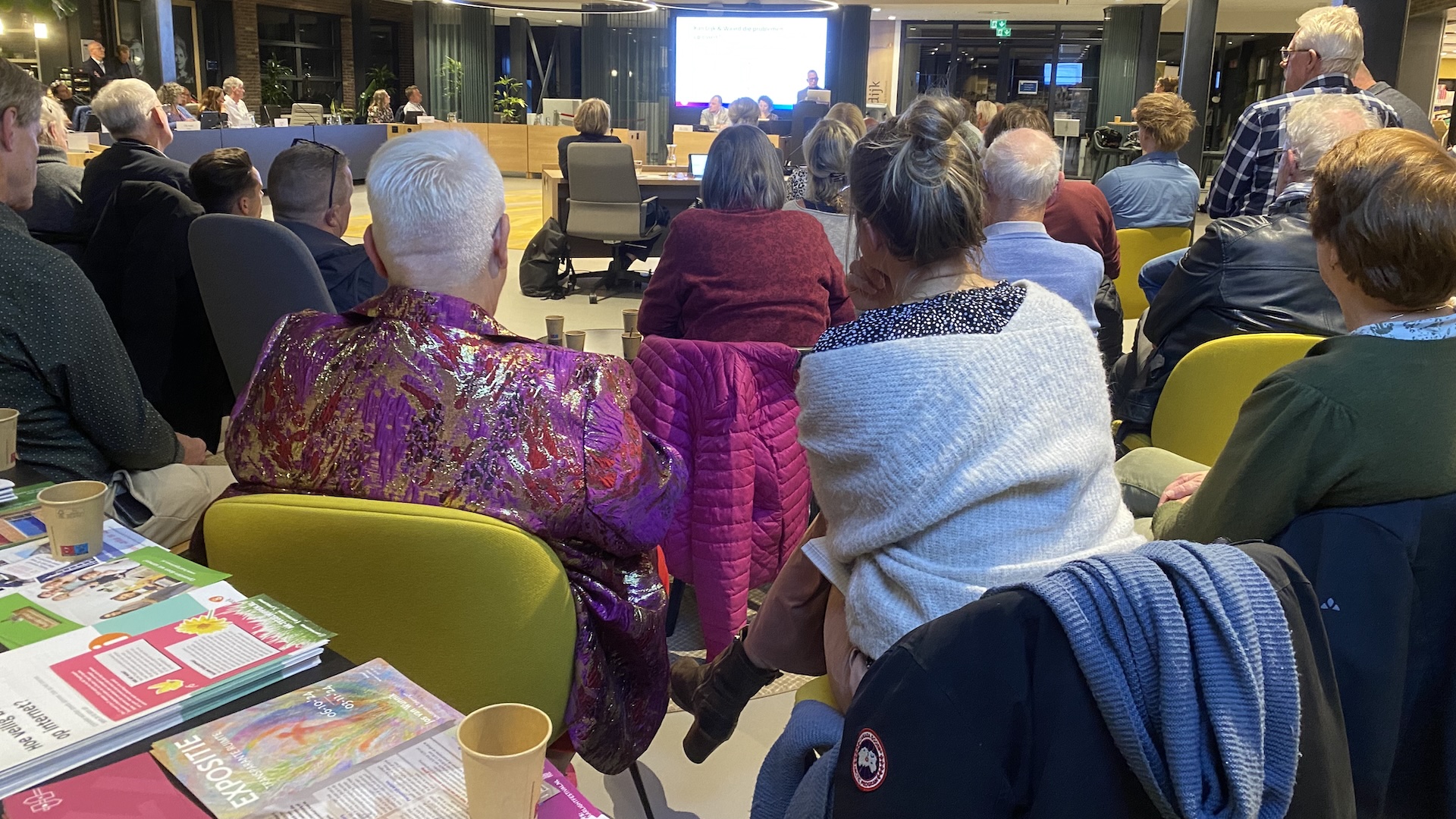 Een groep mensen zit in een vergaderruimte en kijkt naar een presentatie op een scherm aan de voorzijde.