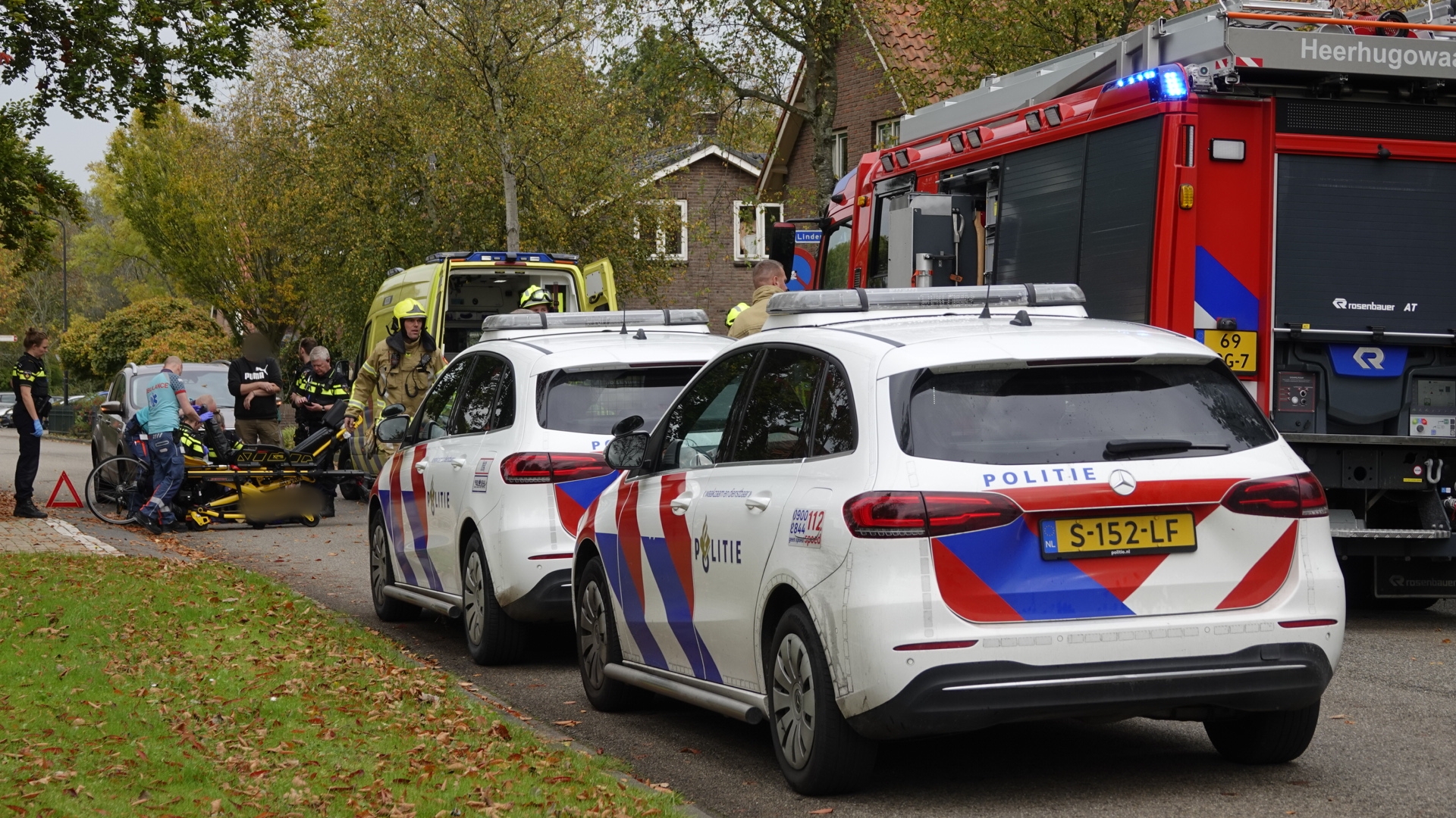 Noodhulp op straat met politieauto's, ambulancepersoneel en brandweerlieden bezig met een incident.