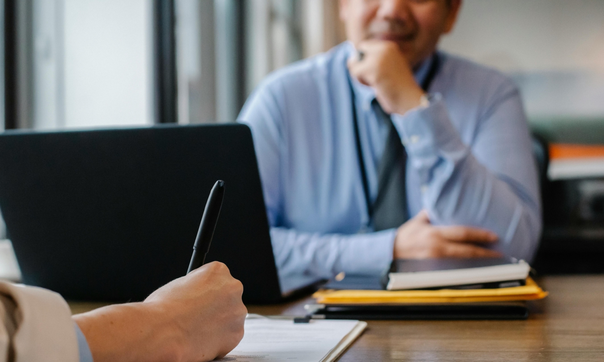 Twee mensen in een gesprek, met een pen op papier en een laptop op tafel.