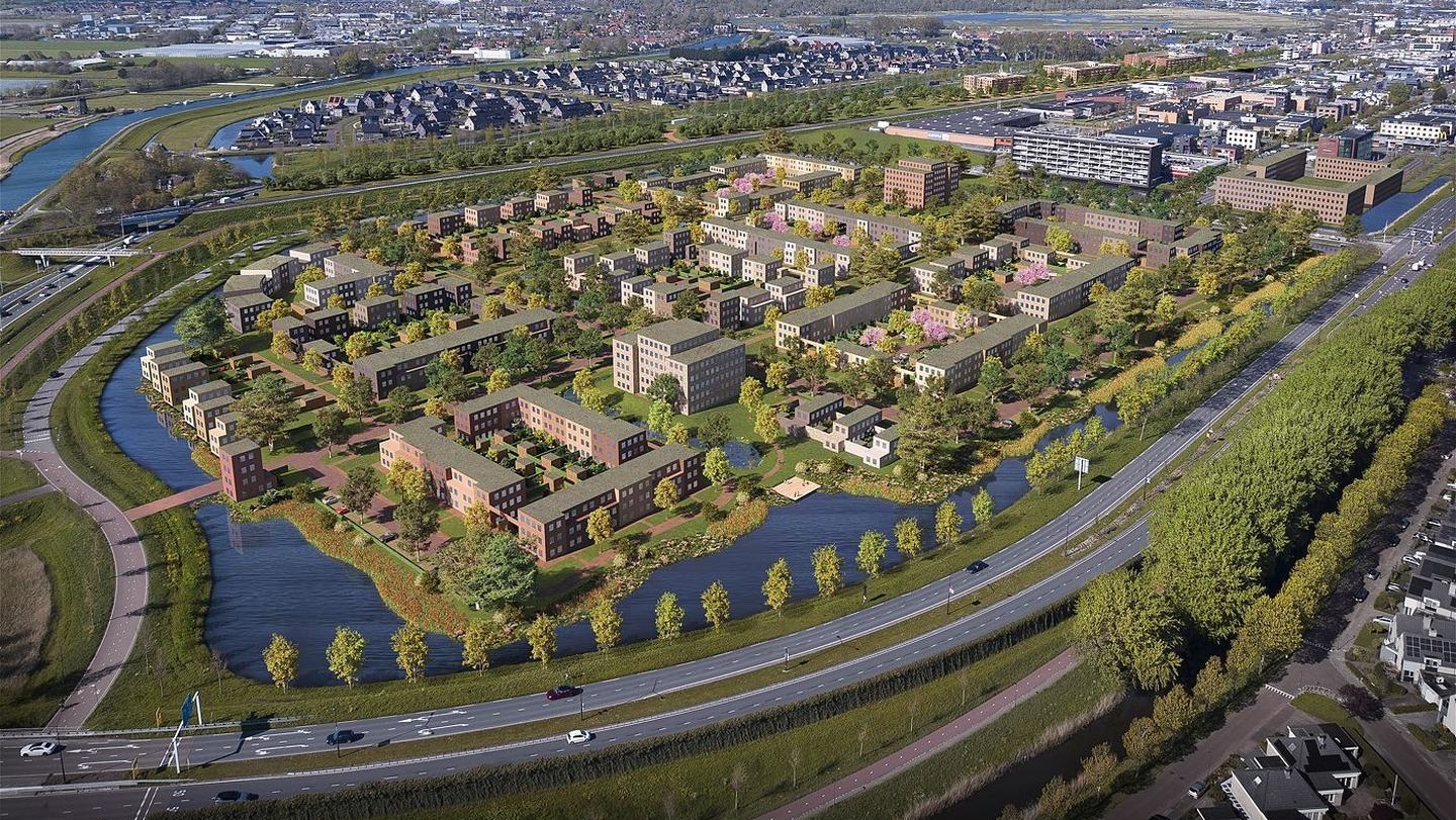 Luchtfoto van een moderne woonwijk met meerdere gebouwen, groene ruimtes en waterpartijen, omringd door wegen en andere infrastructuur.