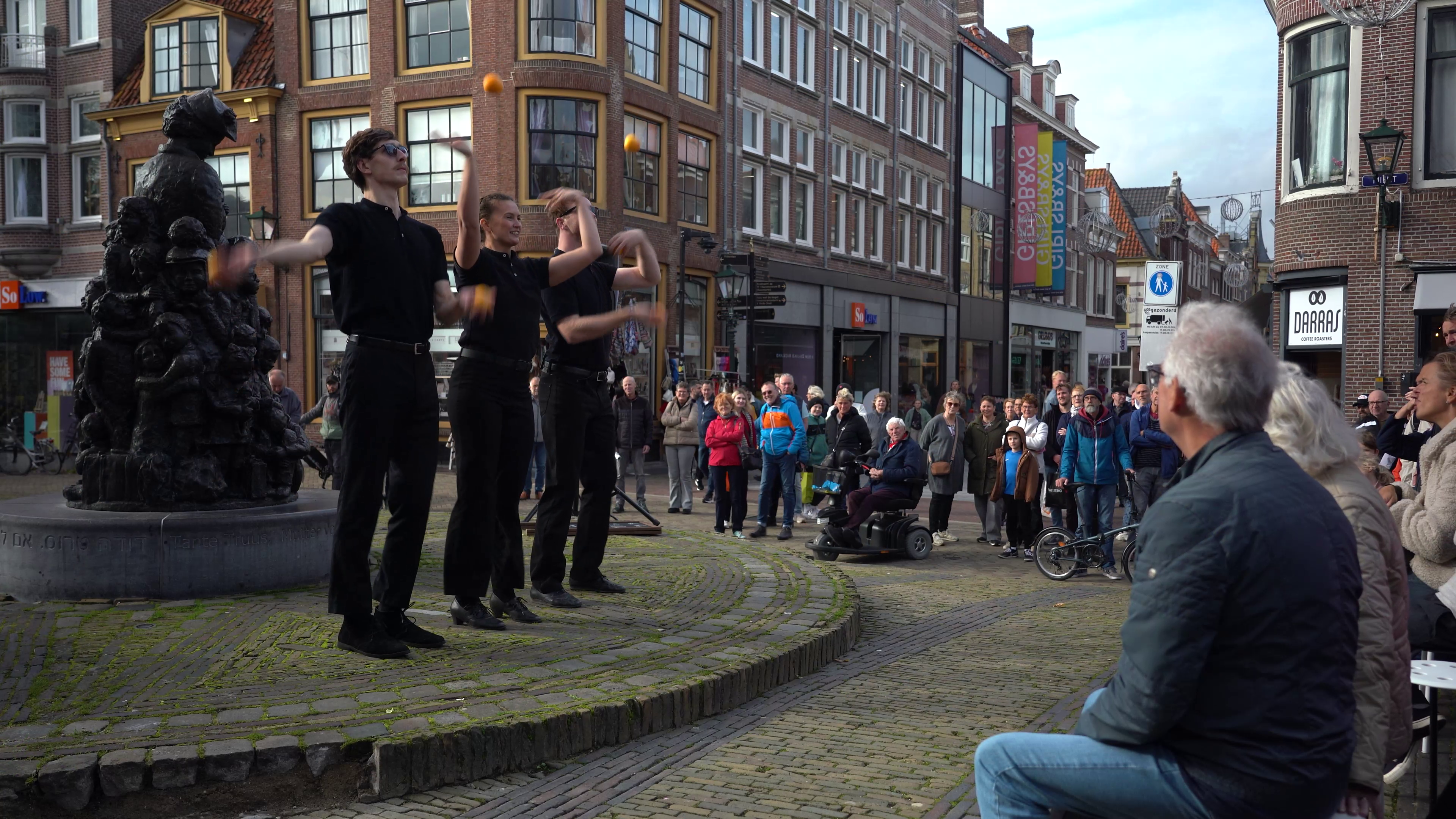 Straatartiesten jongleren voor een publiek op een plein in een stad met historische gebouwen.