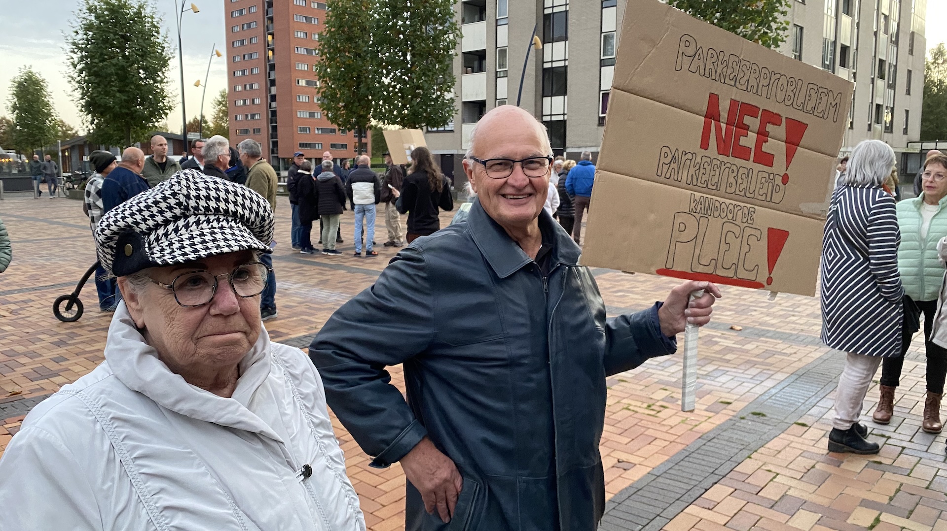 Mensen op een plein met protestborden tegen parkeerbeleid.