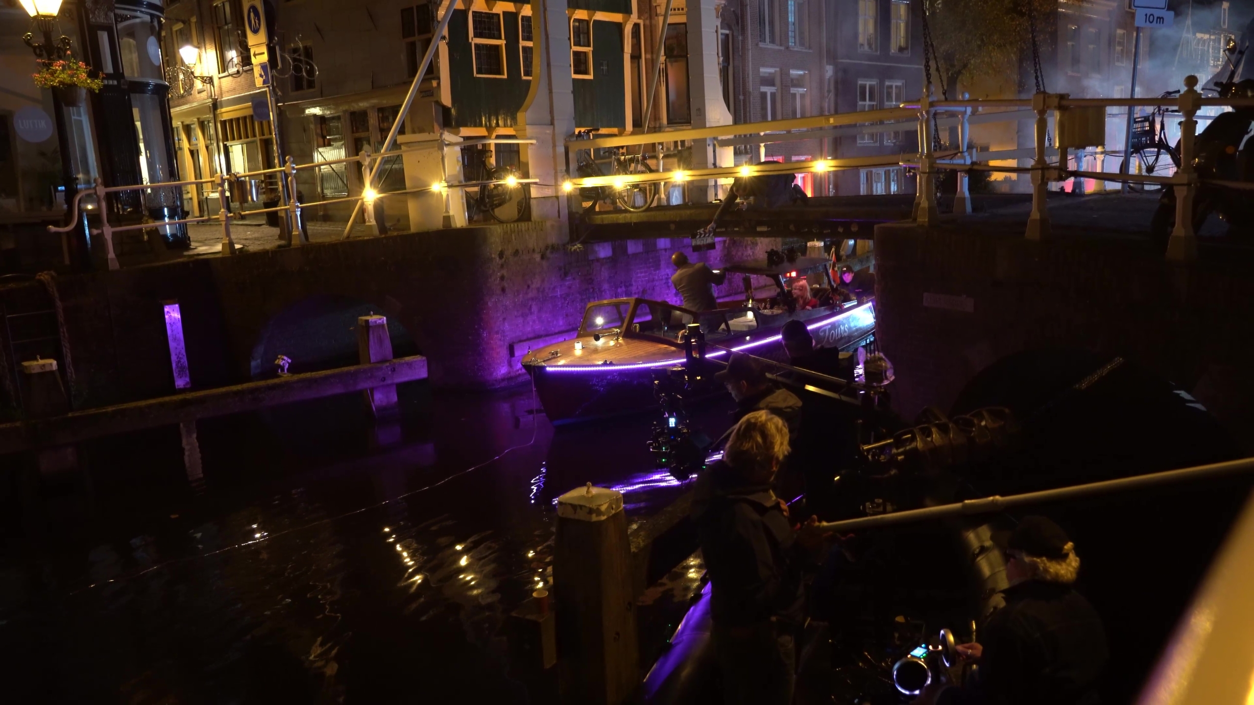 Avondopname van een verlichte boot onder een brug in Alkmaar met mensen op de kade.