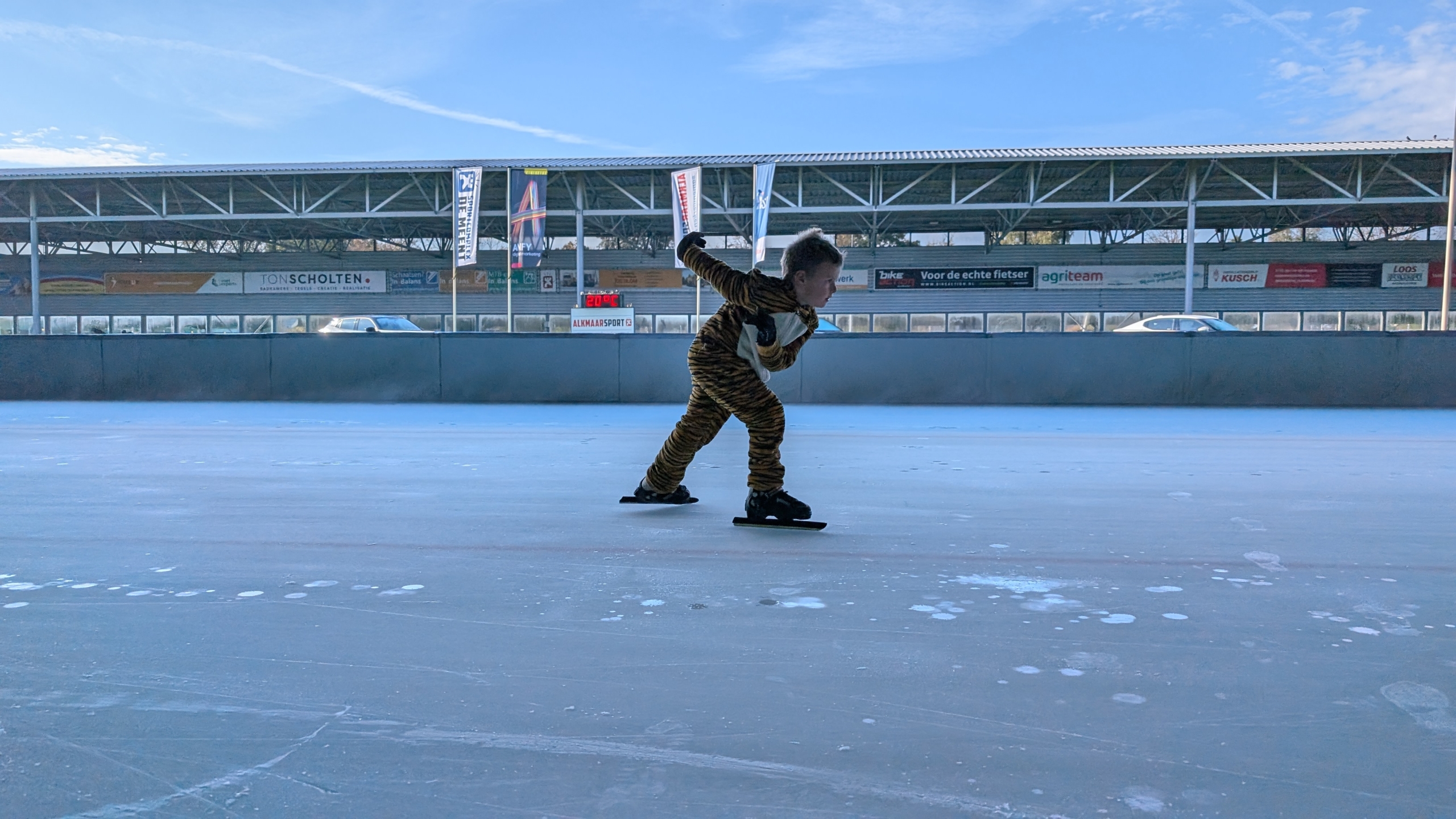 Kind schaatst in een tijgerkostuum op een ijsbaan.