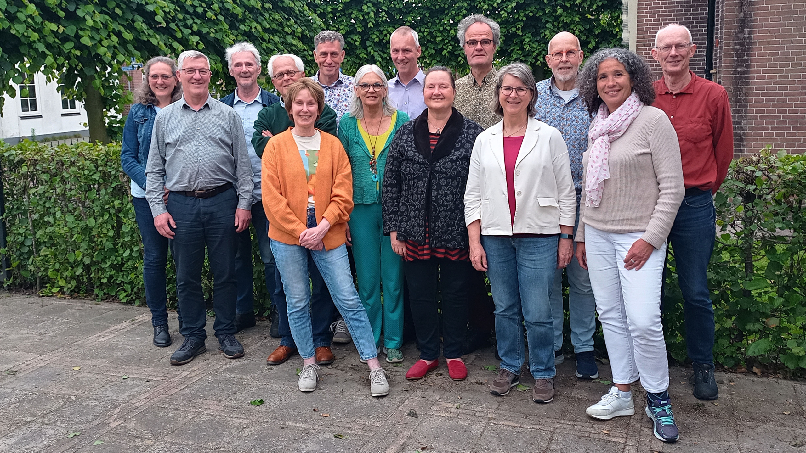 Een groep van vijftien mensen poseert buiten voor een heg.