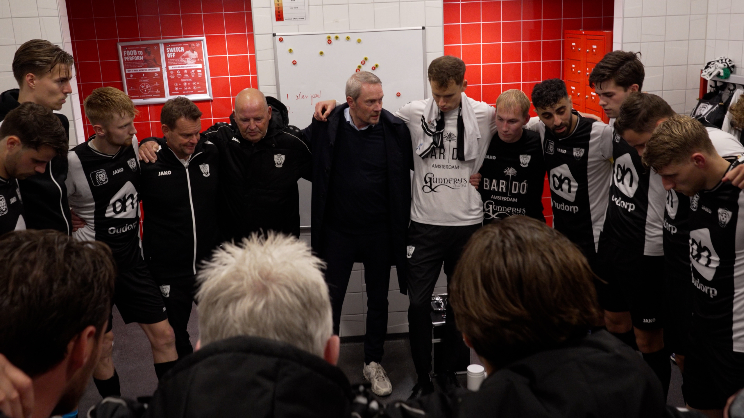 Een voetbalteam in een kleedkamer in een kring met armen om elkaar heen.