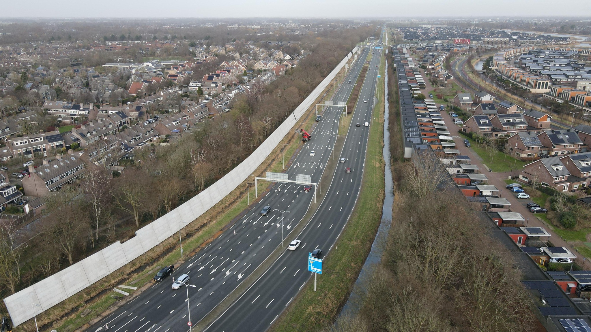 Luchtfoto van een snelweg met meerdere rijstroken, omgeven door woonwijken en een geluidsscherm.