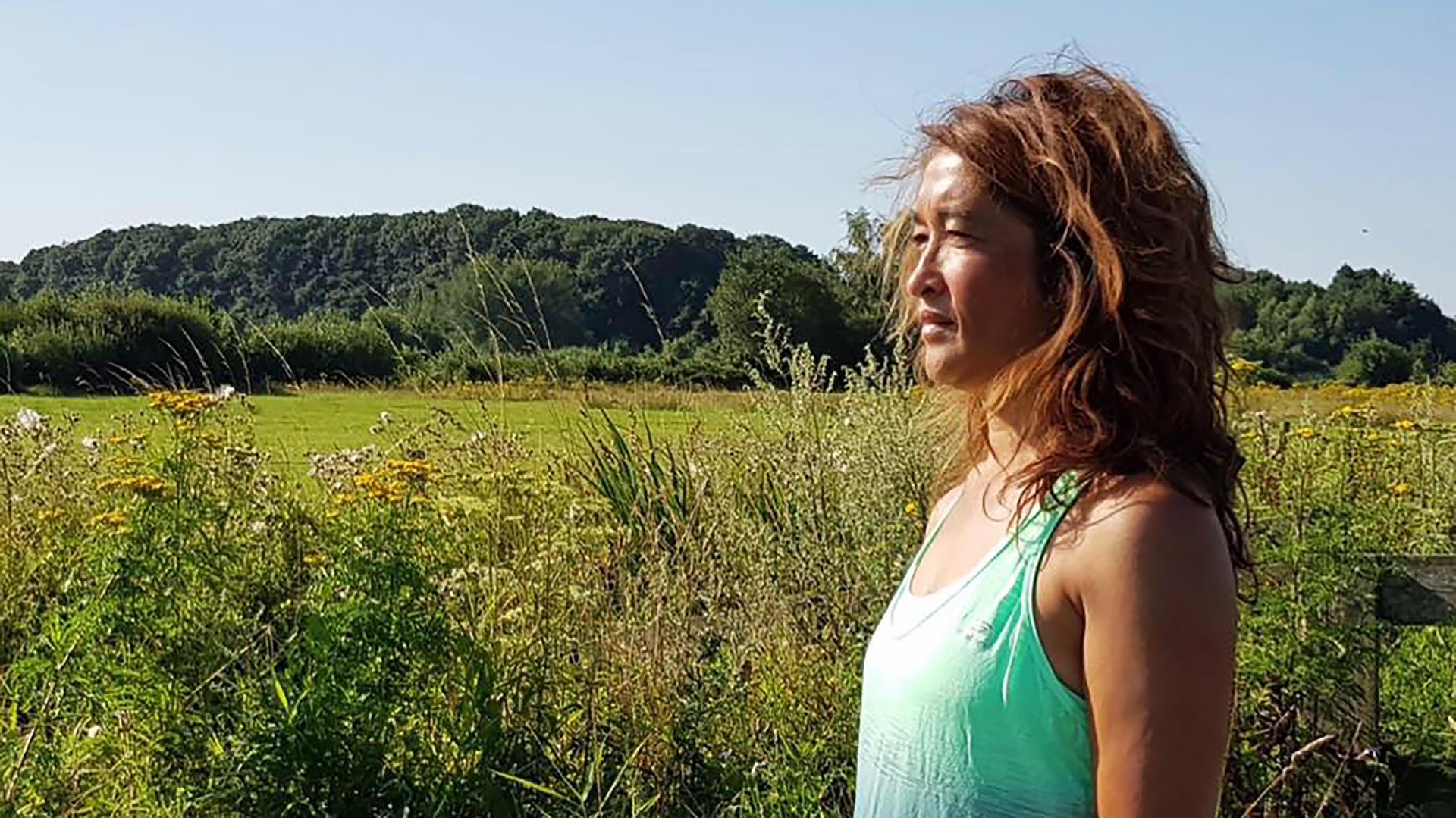 Vrouw in een groen hemdje kijkt naar links in een groene weide met wilde bloemen.