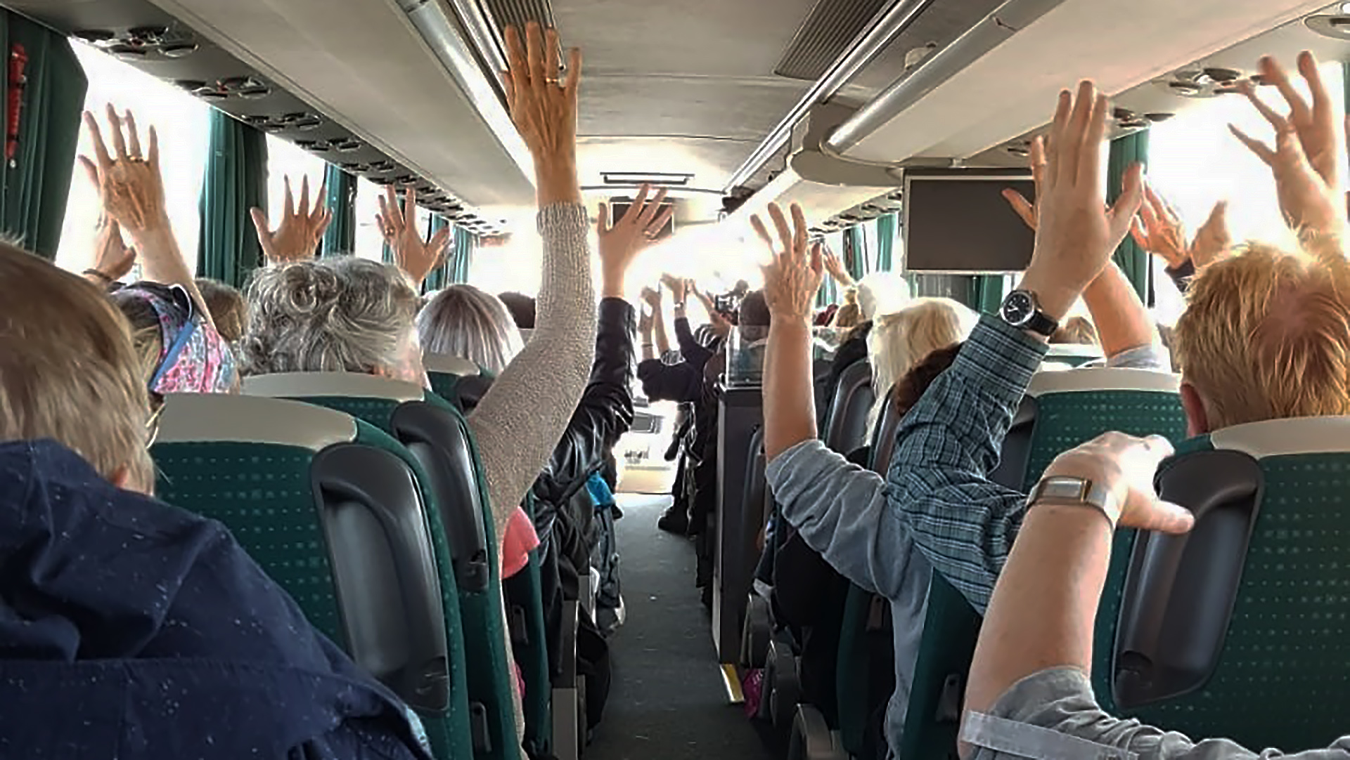 Mensen in een bus steken hun handen in de lucht.