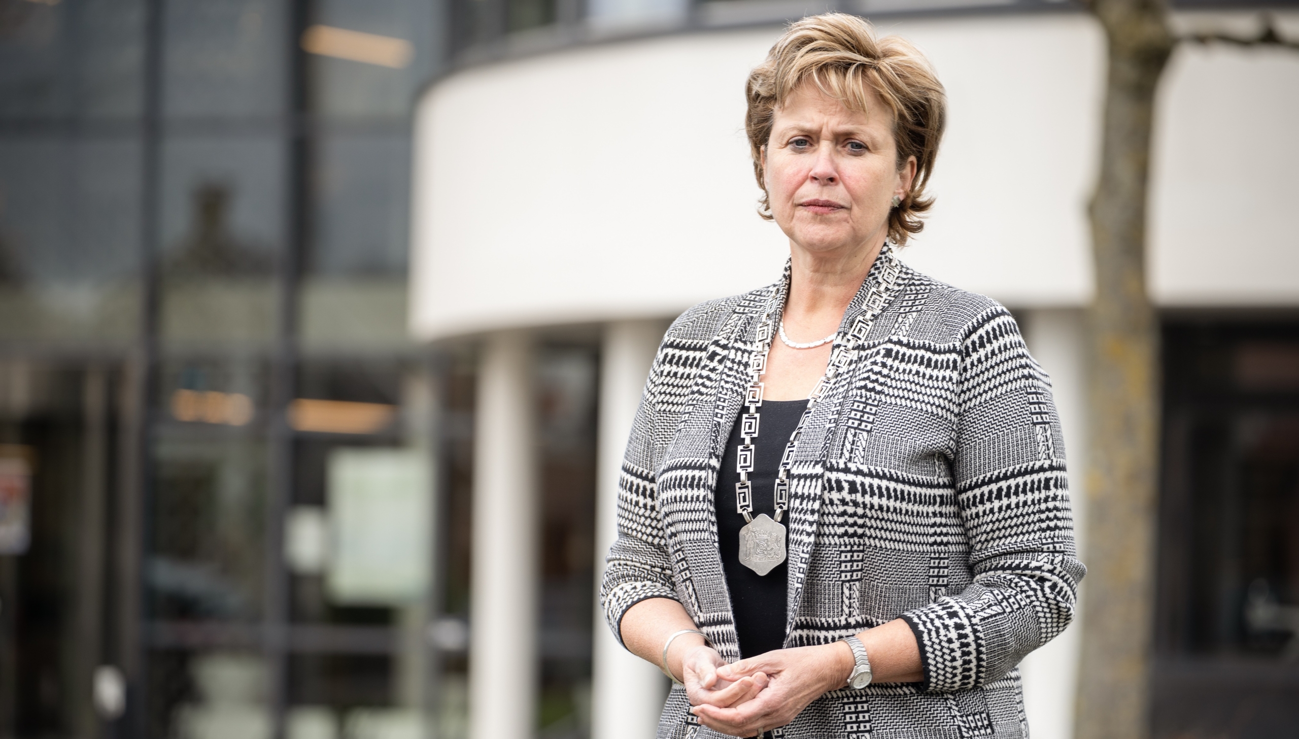 Vrouw in een grijze blazer staat voor een modern gebouw.