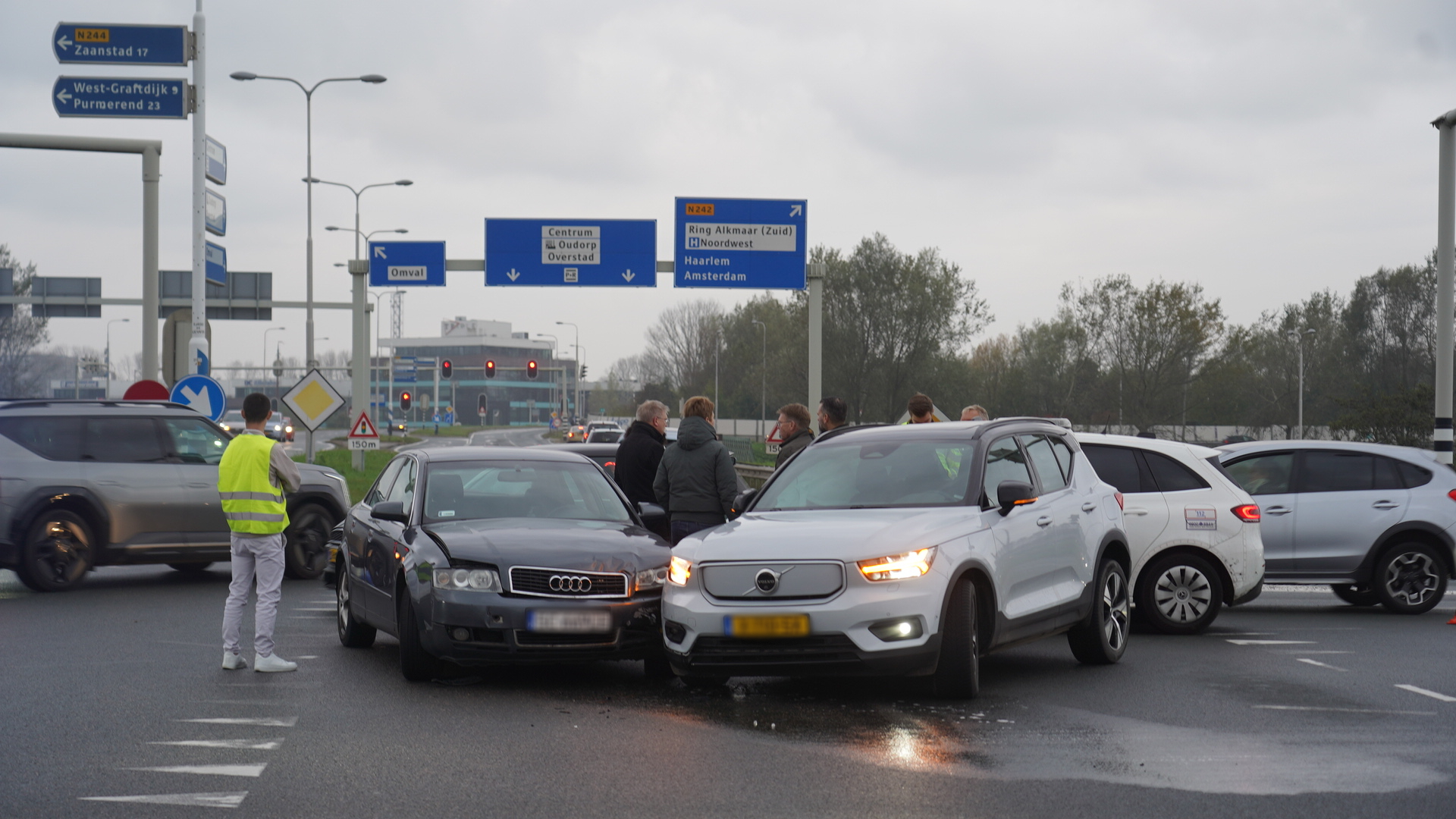 Twee auto's betrokken bij een botsing op een wegkruising, met omstanders die de situatie bekijken.