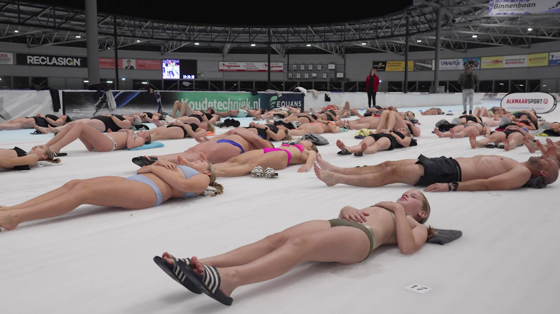 Mensen in badkleding liggen op de grond van een indoor ijsbaan.