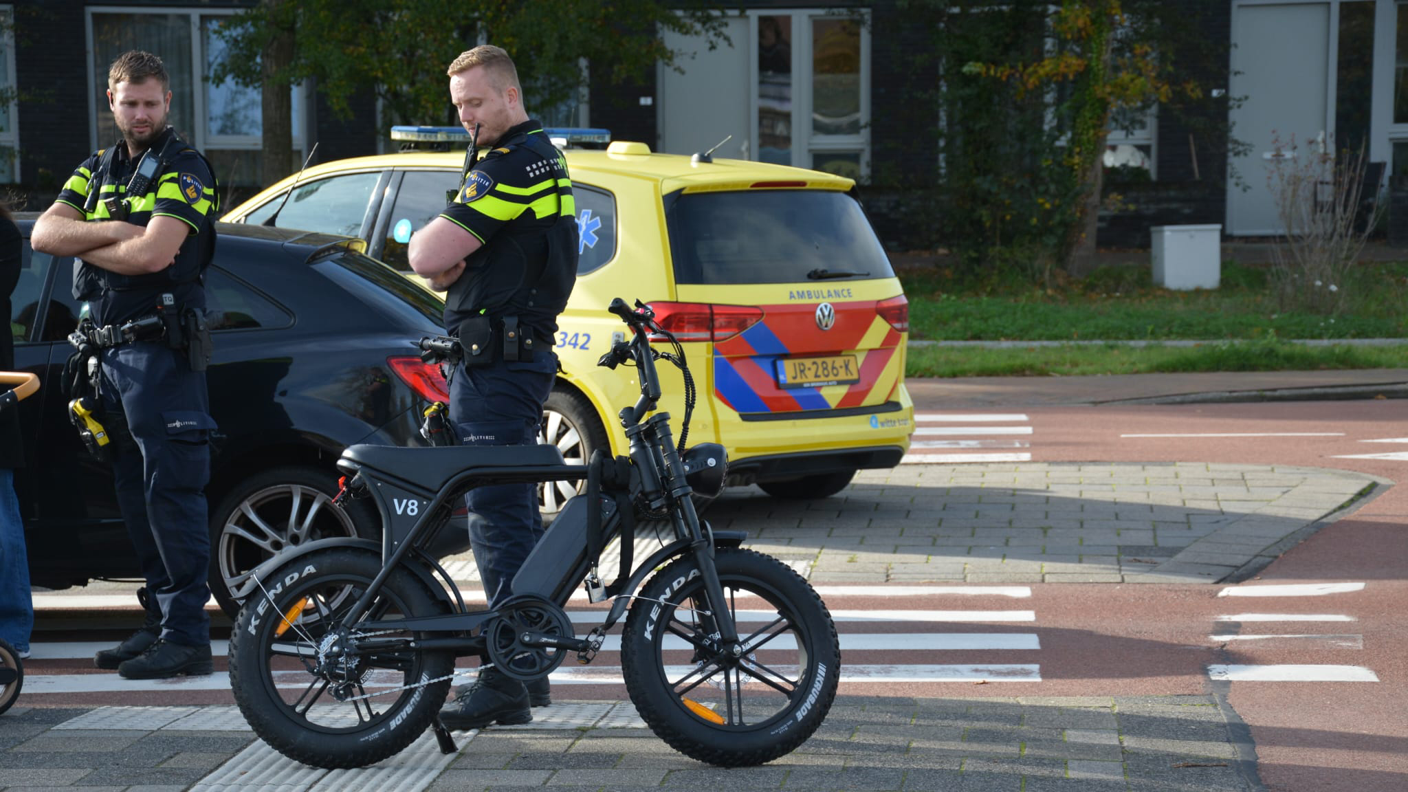 Twee politieagenten naast een elektrische fiets en een geparkeerde ambulance.