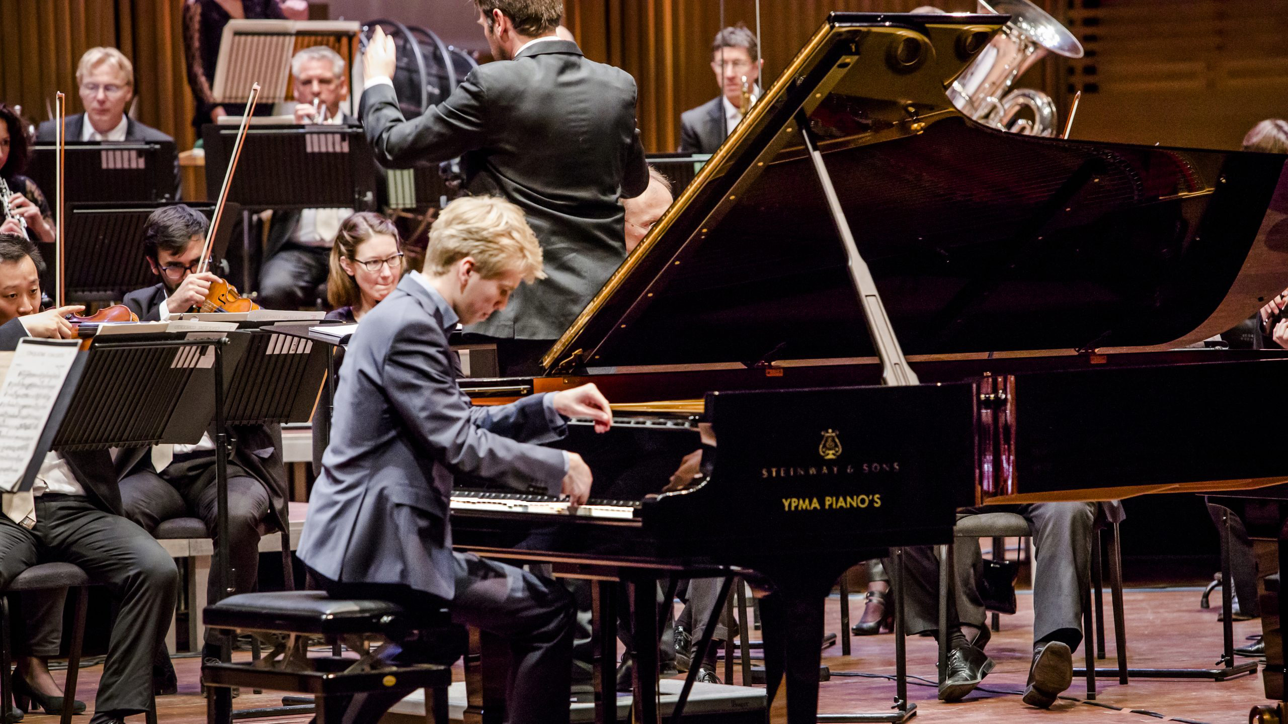 Pianist speelt op een Steinway & Sons vleugel met orkest op de achtergrond.